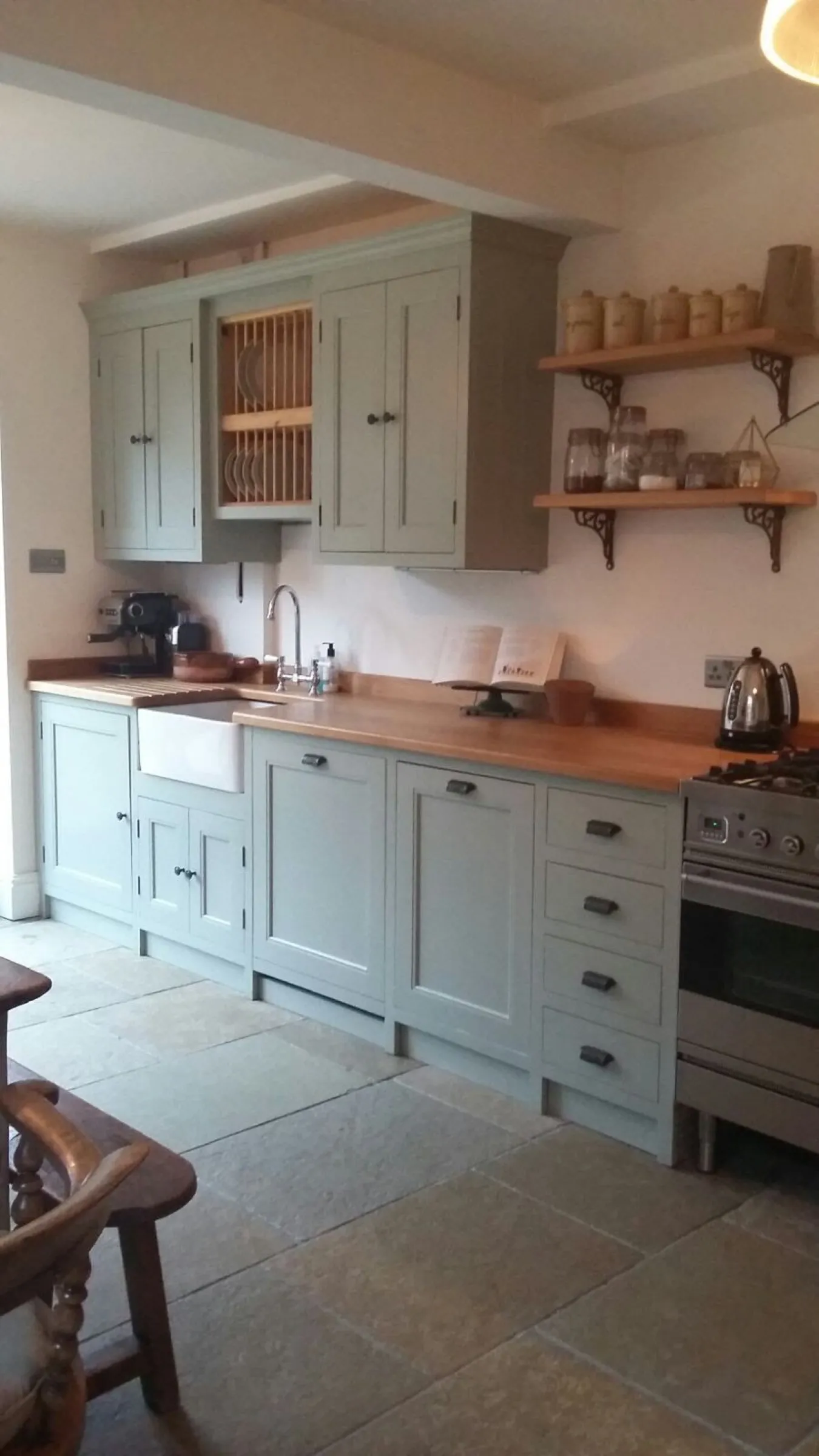 Sage green Shaker kitchen with oak worktops, Belfast sink, plate rack and stainless steel range cooker on a flagstone floor
