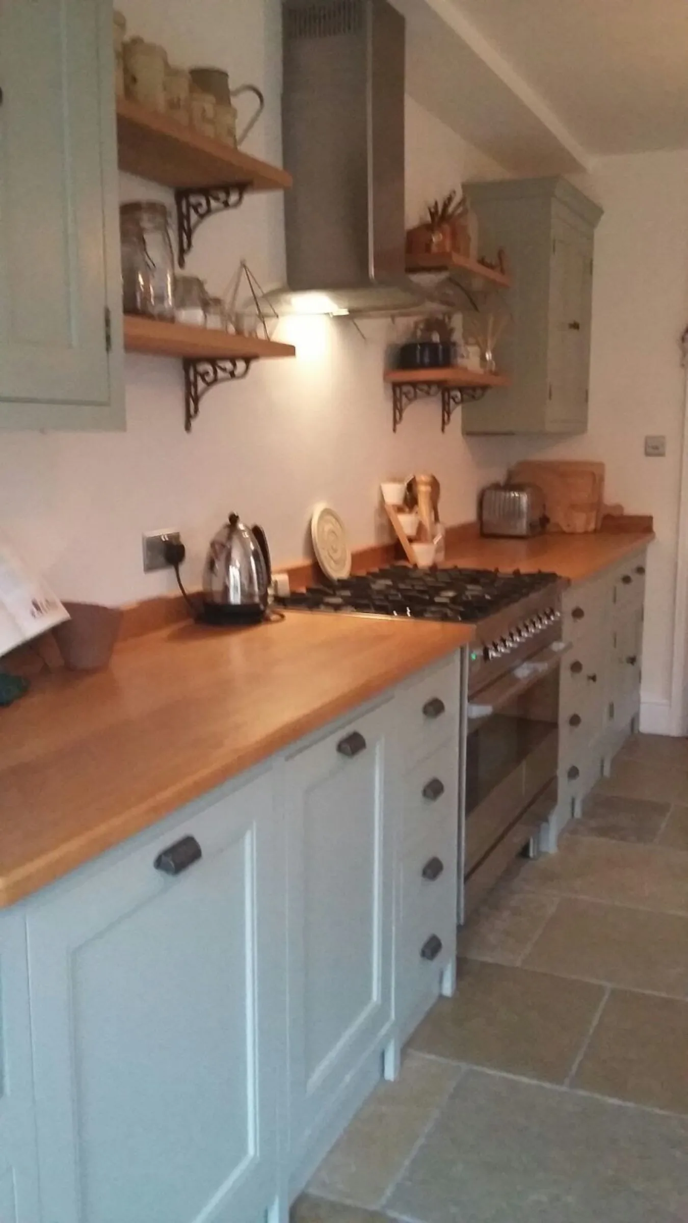 Oak worktop run leading to the range cooker and chimney hood, with open oak shelves on decorative cast iron brackets