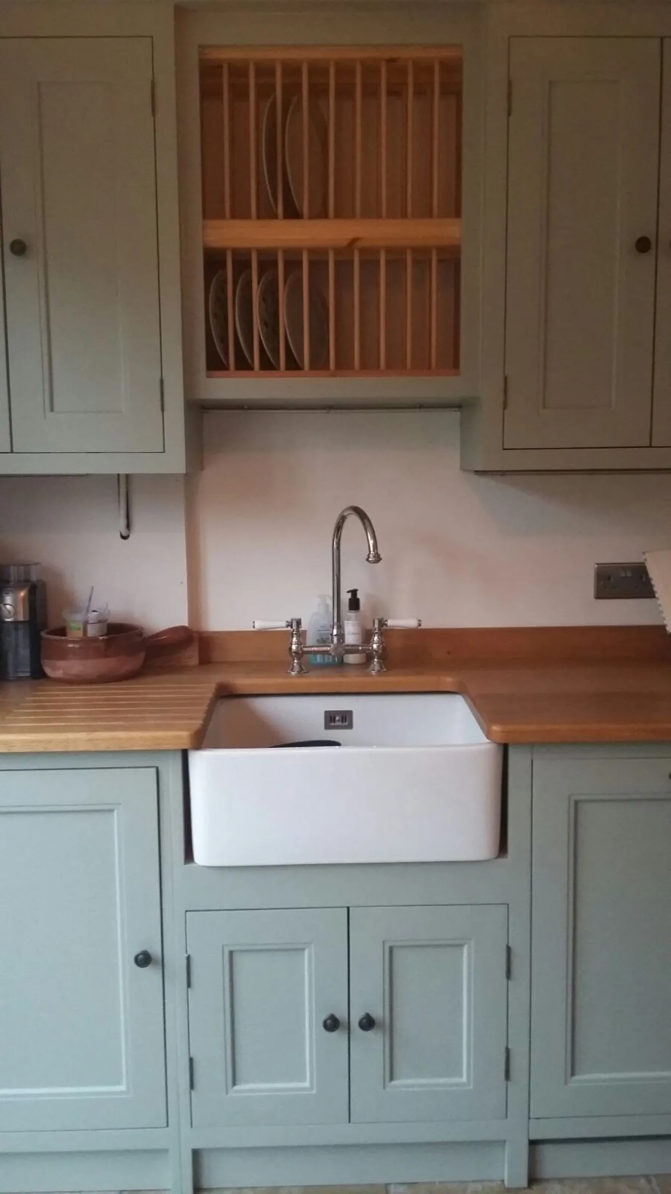 Belfast sink with chrome bridge tap beneath a bespoke wooden plate rack, with draining grooves cut into the oak worktop