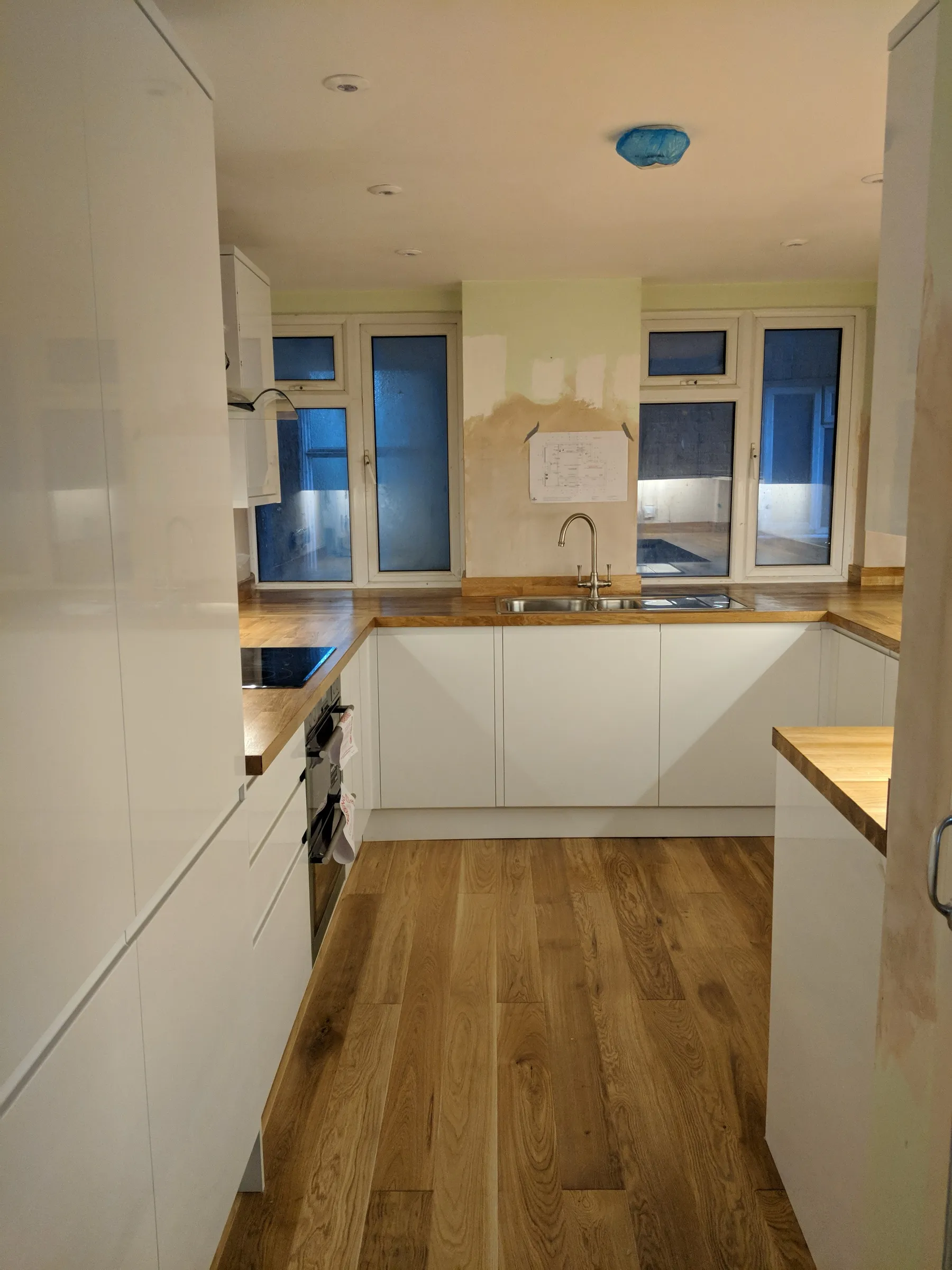 U-shaped kitchen with gloss white handleless units, solid oak worktops, oak flooring, built-in oven and black glass hob, photographed just after installation