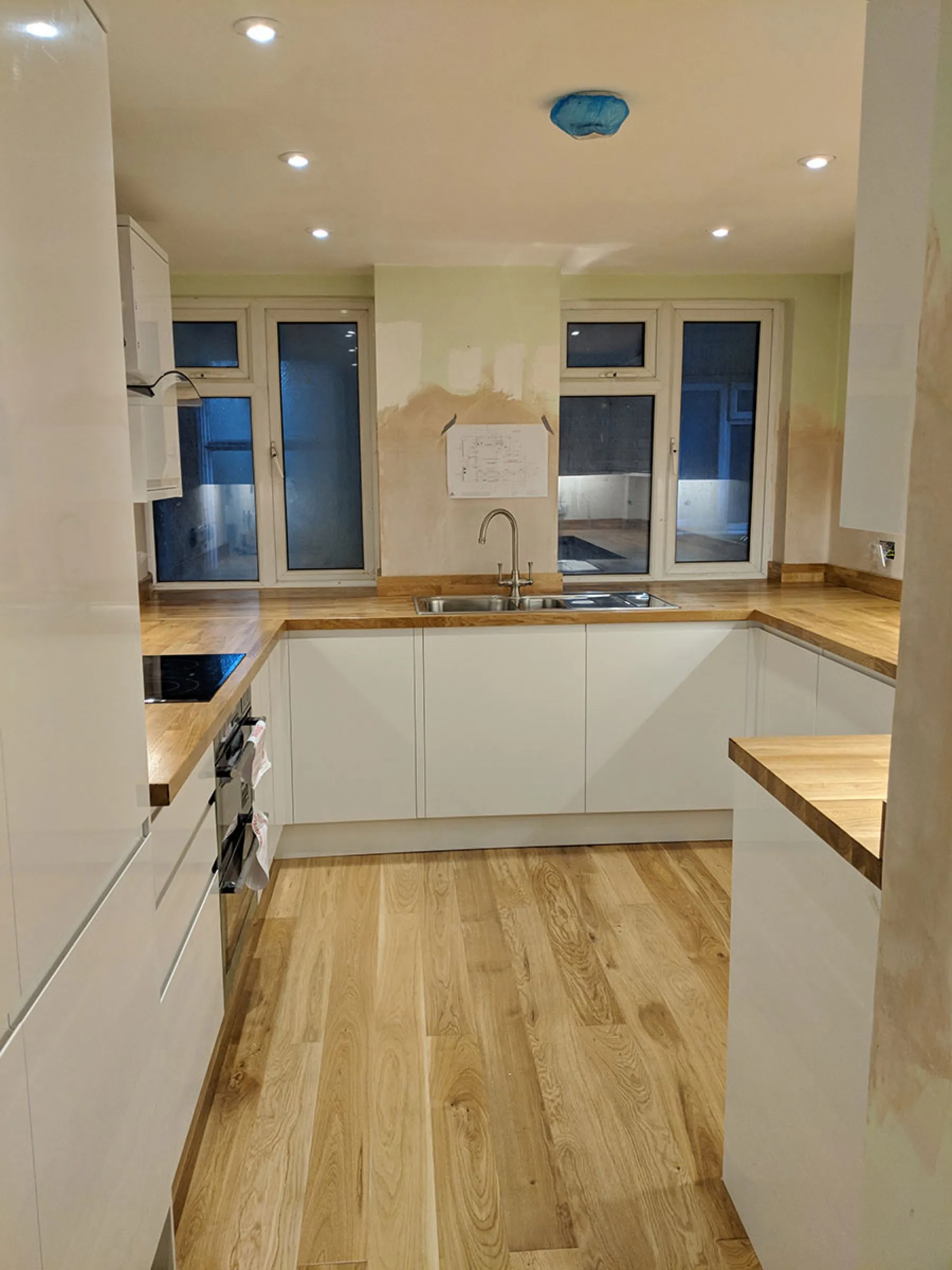 U-shaped run of white handleless units with oak worktops and inset sink beneath the windows, mid-renovation