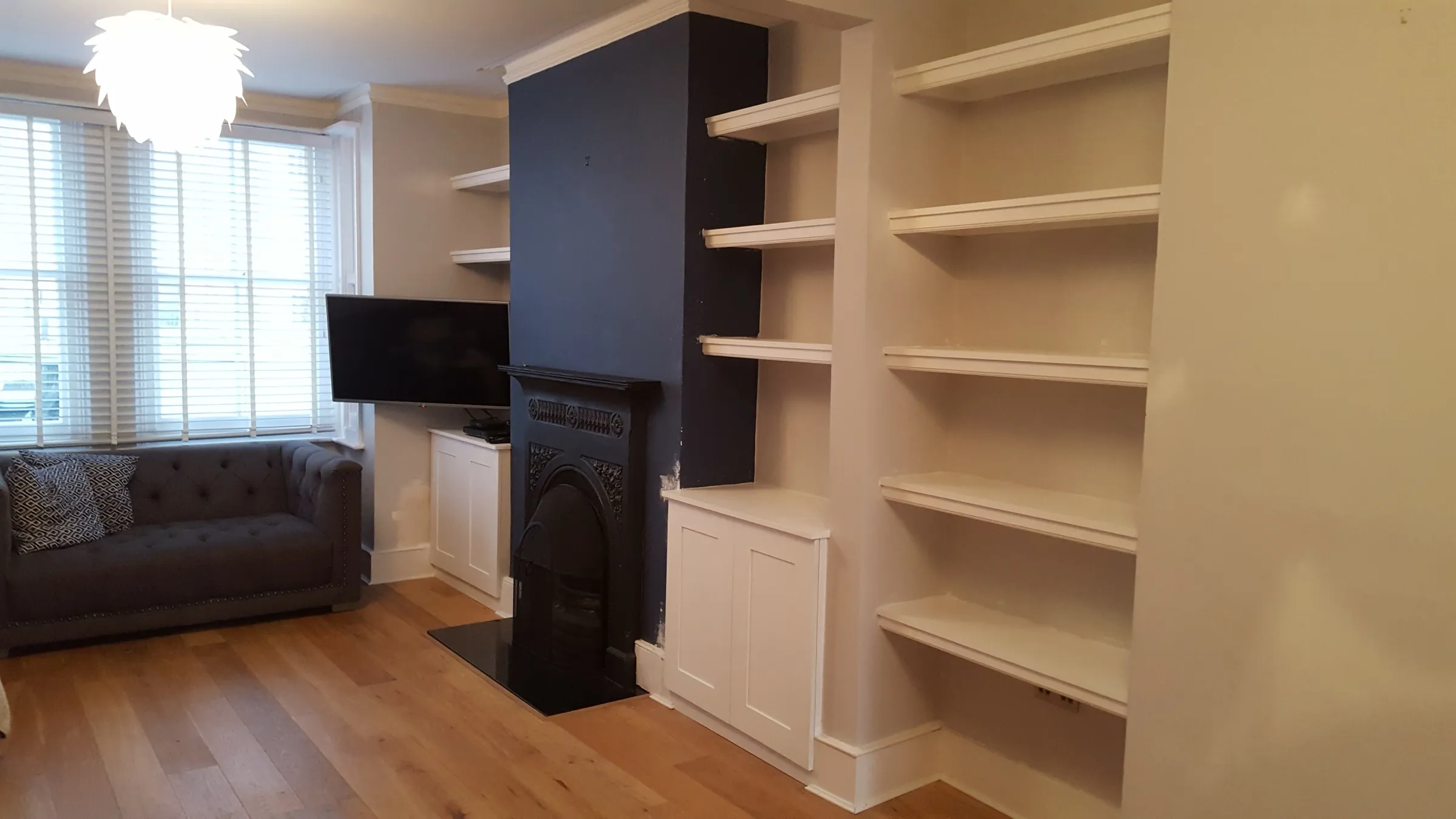 Painted alcove units with open shelving and cupboard bases flanking a navy chimney breast and Victorian cast-iron fireplace in a living room