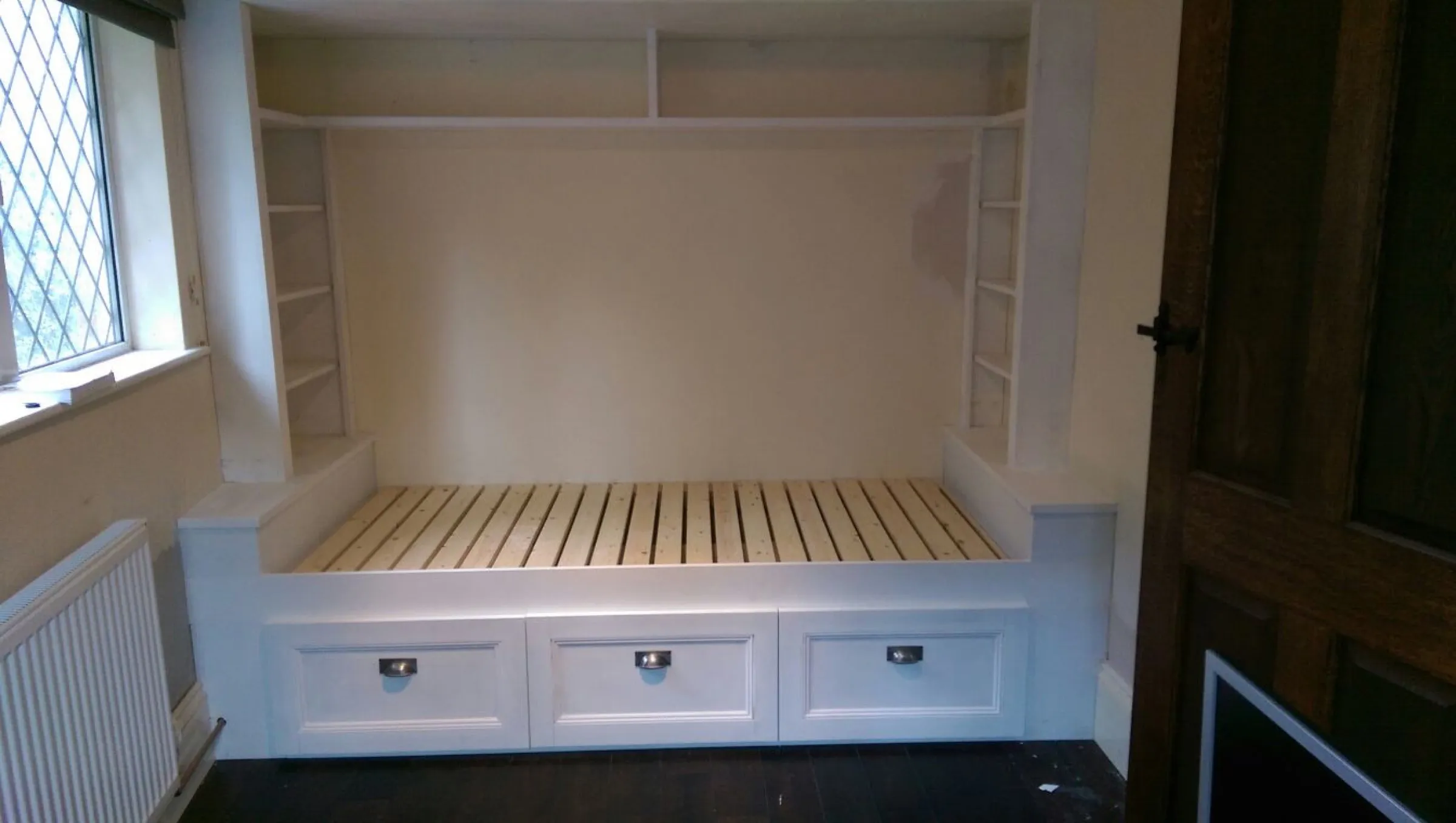 Built-in day bed with slatted base, three deep storage drawers and a shelved surround, photographed during installation