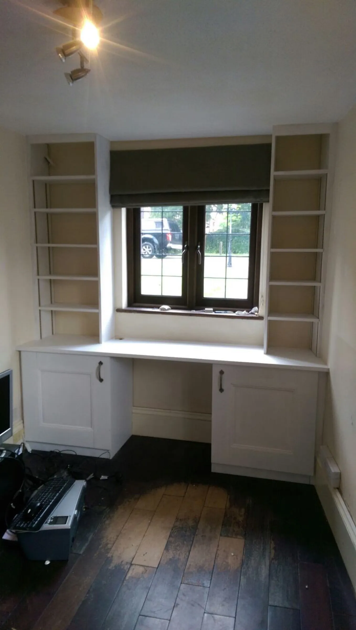 Fitted home study with painted desk, cupboards and tall open shelving built around a leaded cottage window