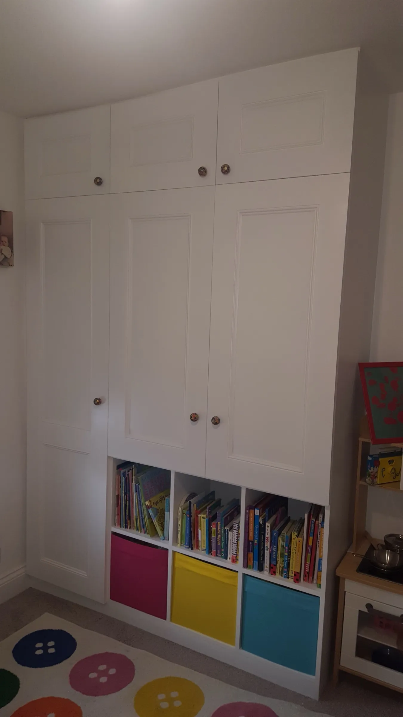 Floor-to-ceiling fitted wardrobes in a child's bedroom with integrated cube bookshelves and colourful fabric storage boxes