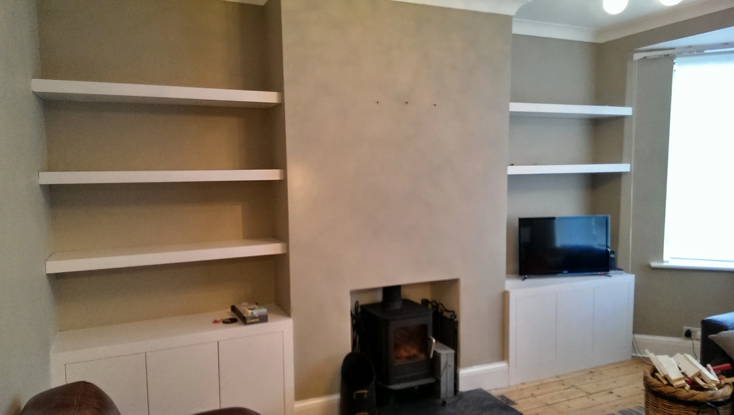 Chunky floating alcove shelves and low cupboards either side of a chimney breast with a wood-burning stove