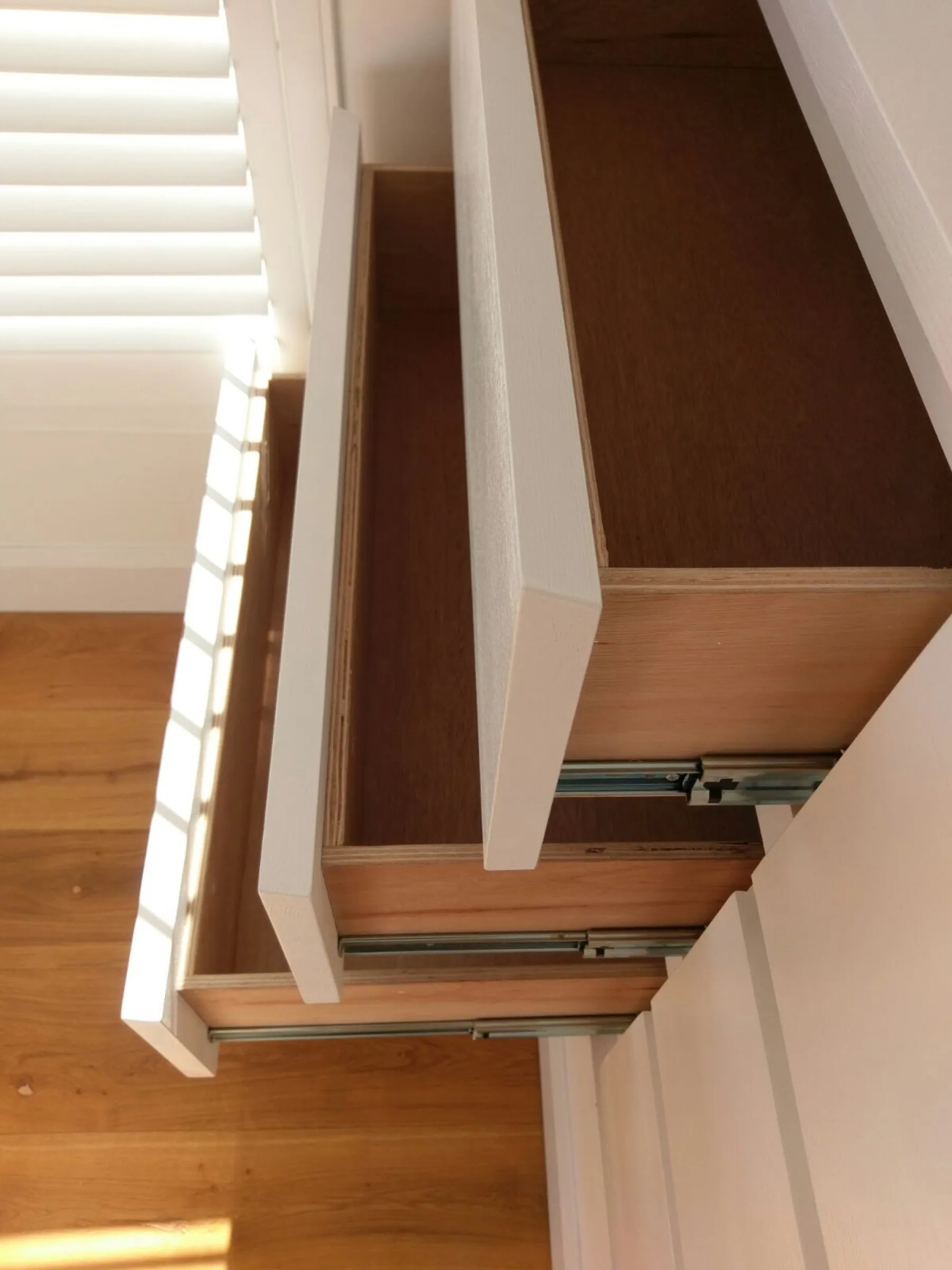 Handleless fitted drawer unit with floating shelves shaped around sloping eaves in a loft bedroom