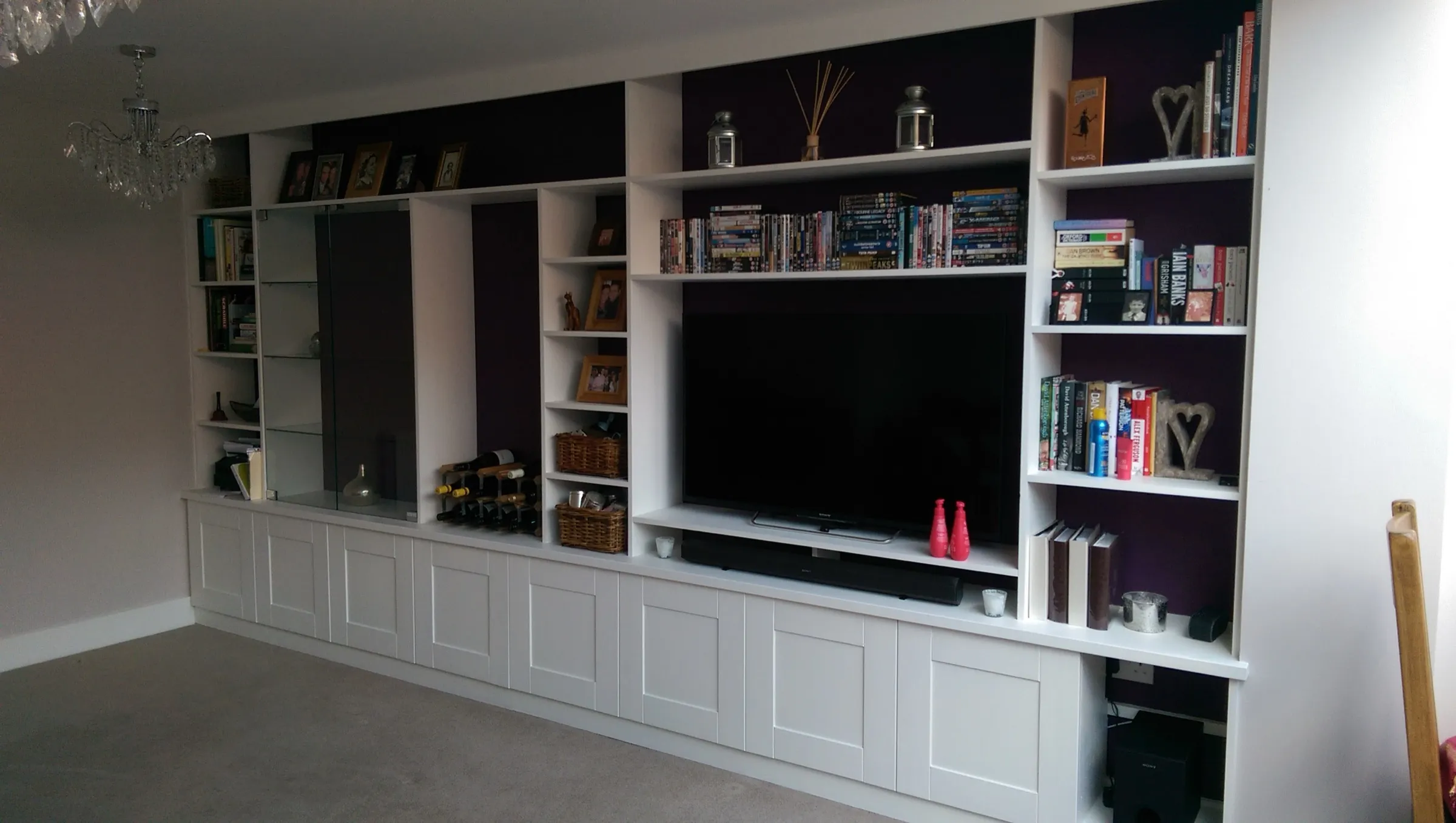 Full-width fitted media wall with Shaker cupboards, recessed TV and display shelving against an aubergine backdrop