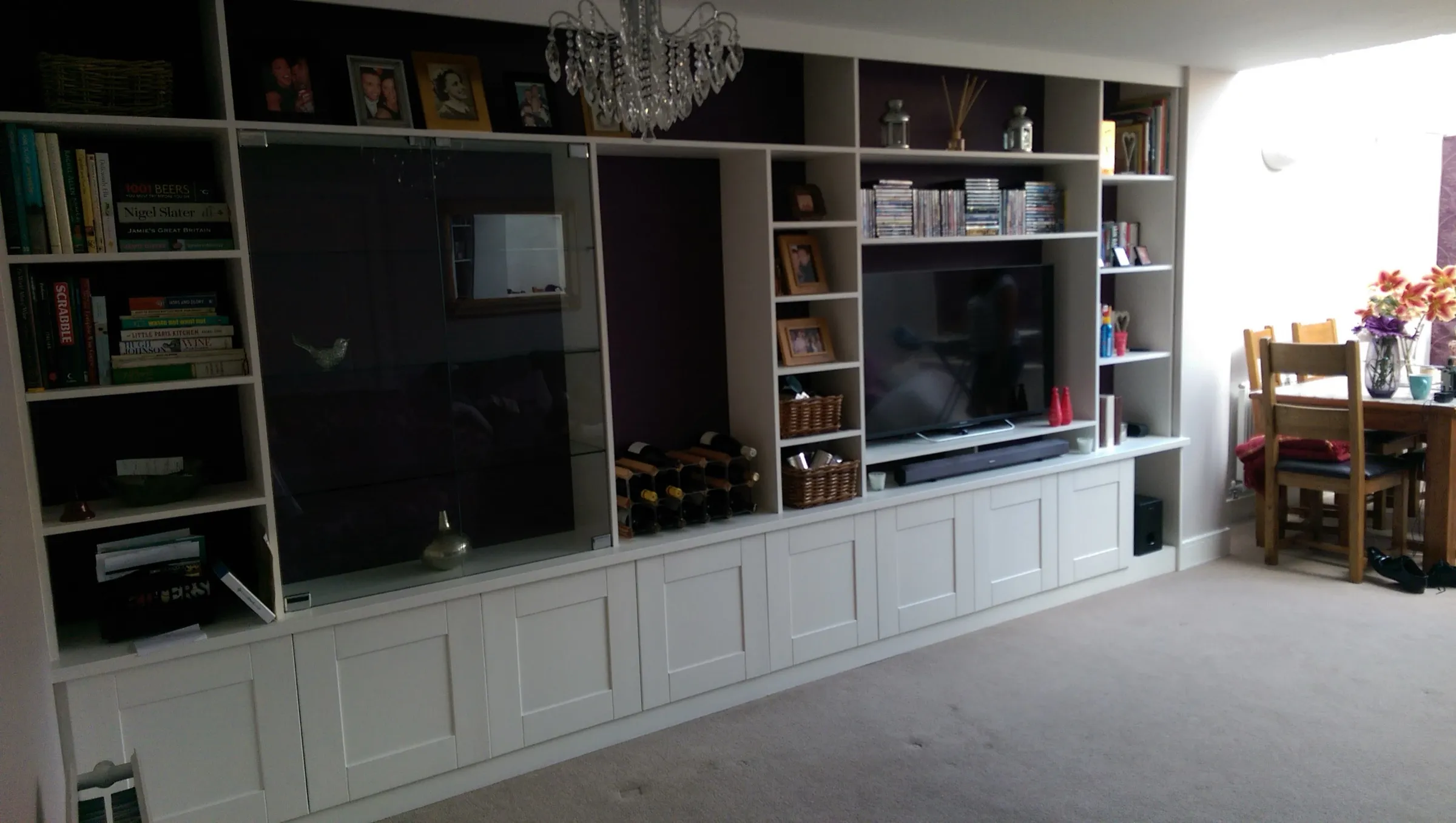 Fitted media wall with sliding glass display cabinet, wine rack and open shelving, viewed from the dining area