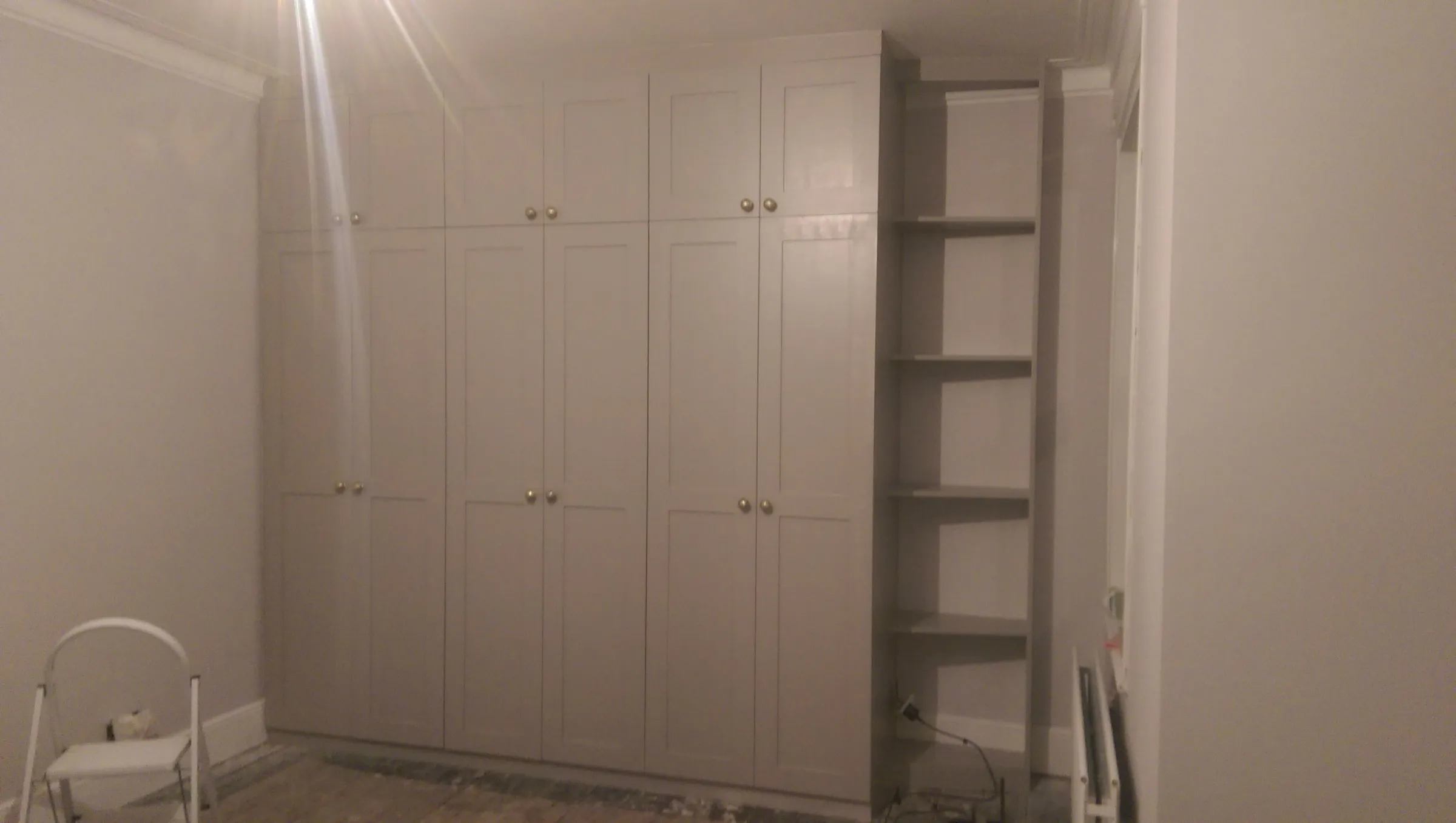 Full-height fitted wardrobes in warm grey with Shaker doors, top boxes and an open shelving return, newly installed