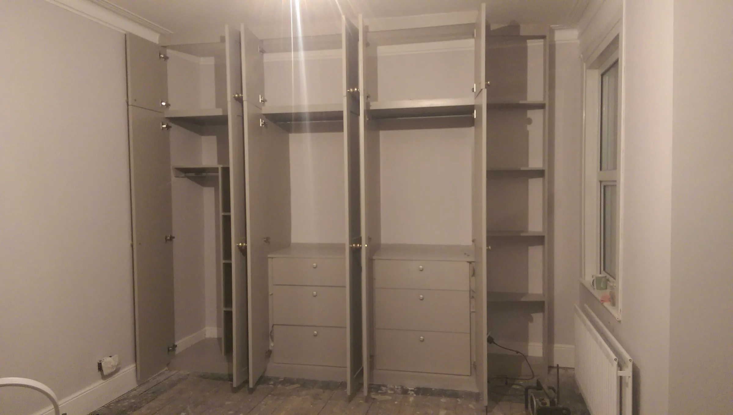 Fitted wardrobes with doors open, revealing internal drawer chests, hanging rails and adjustable shelving during fit-out