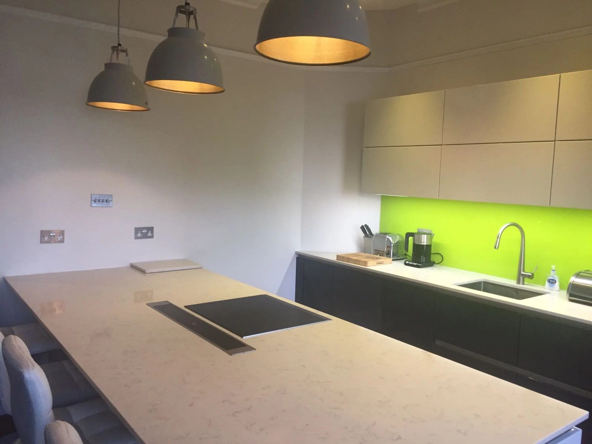 Marble-effect quartz island with flush induction hob and downdraught extractor, grey gloss units and a lime green glass splashback