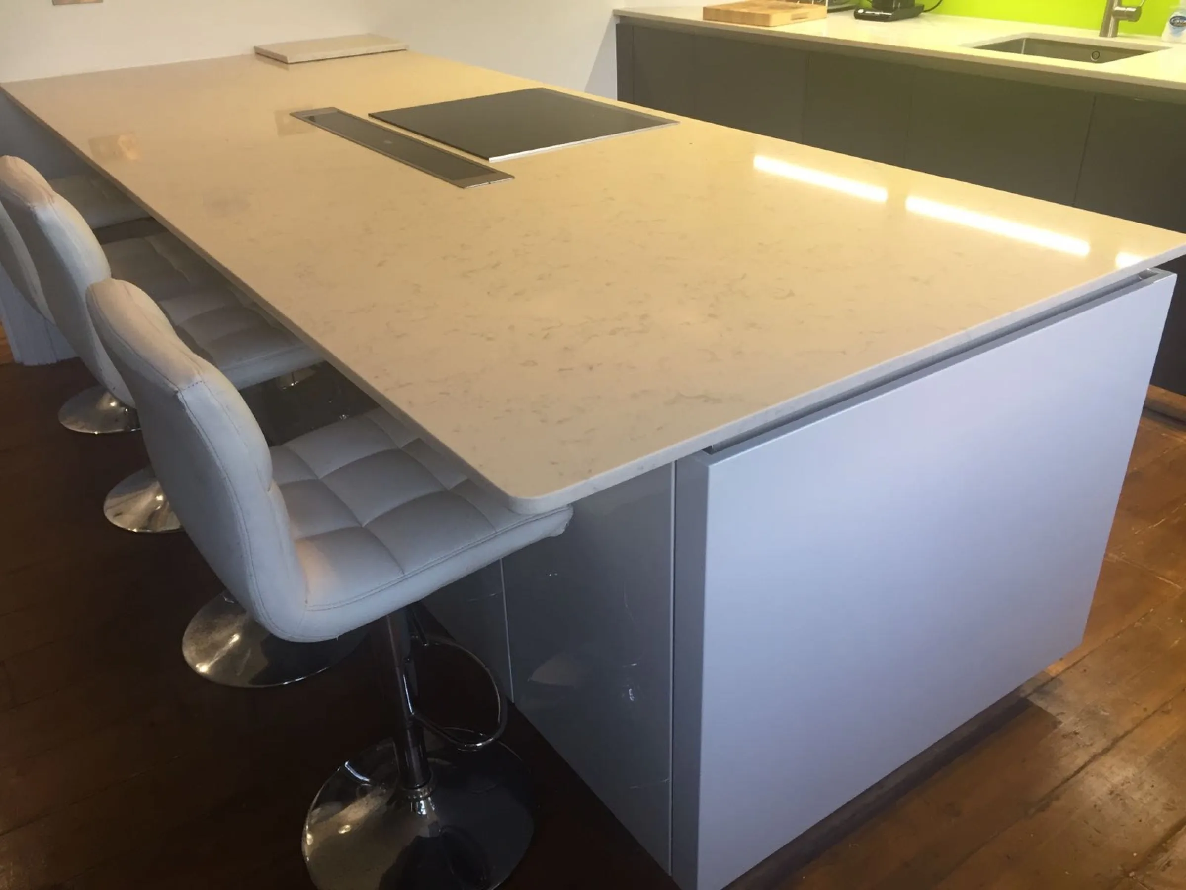 Close-up of the quartz-topped island with quilted white leather bar stools and grey gloss handleless panels