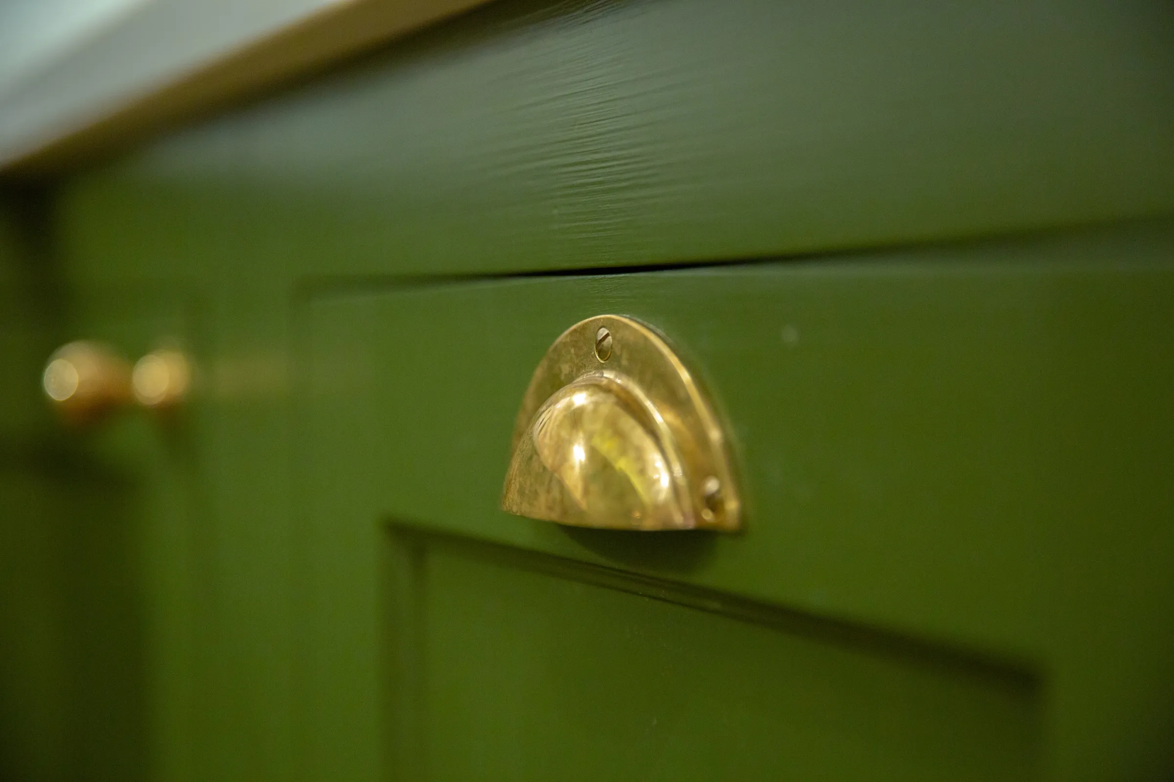 Close-up of an aged brass cup handle on a hand-painted green drawer front