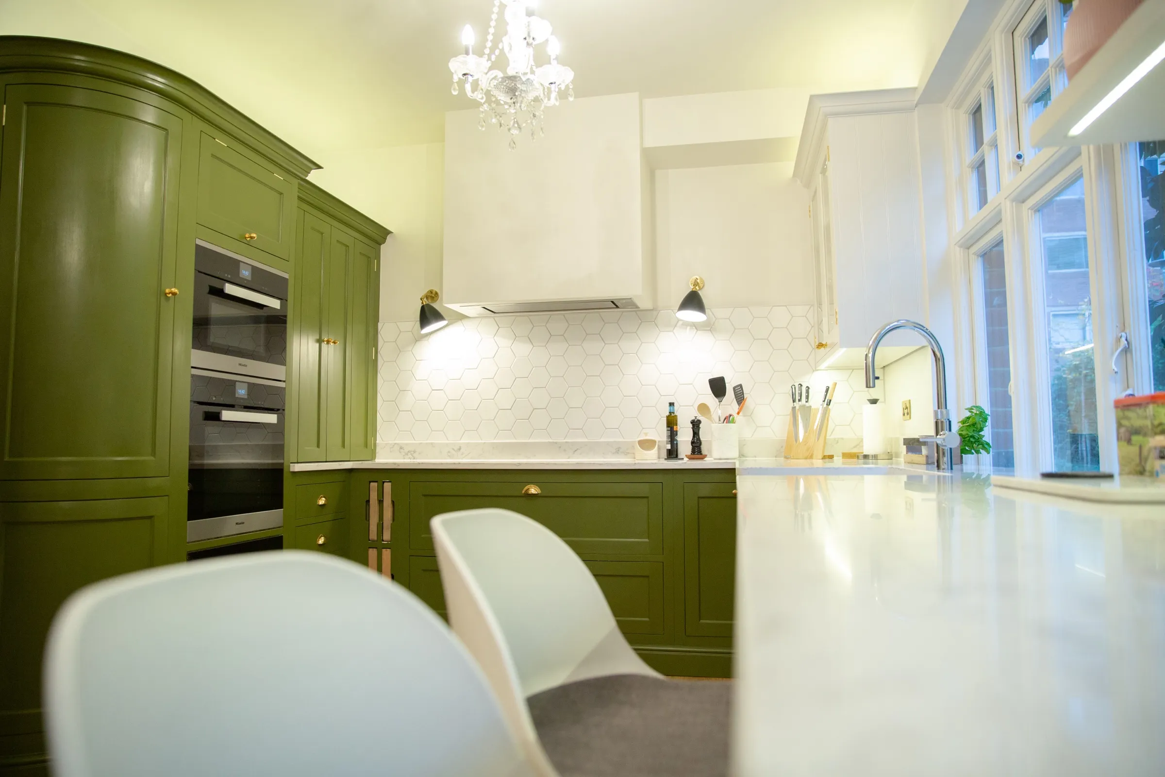 View from the breakfast bar seats across the quartz worktop towards the curved oven cabinet and chandelier