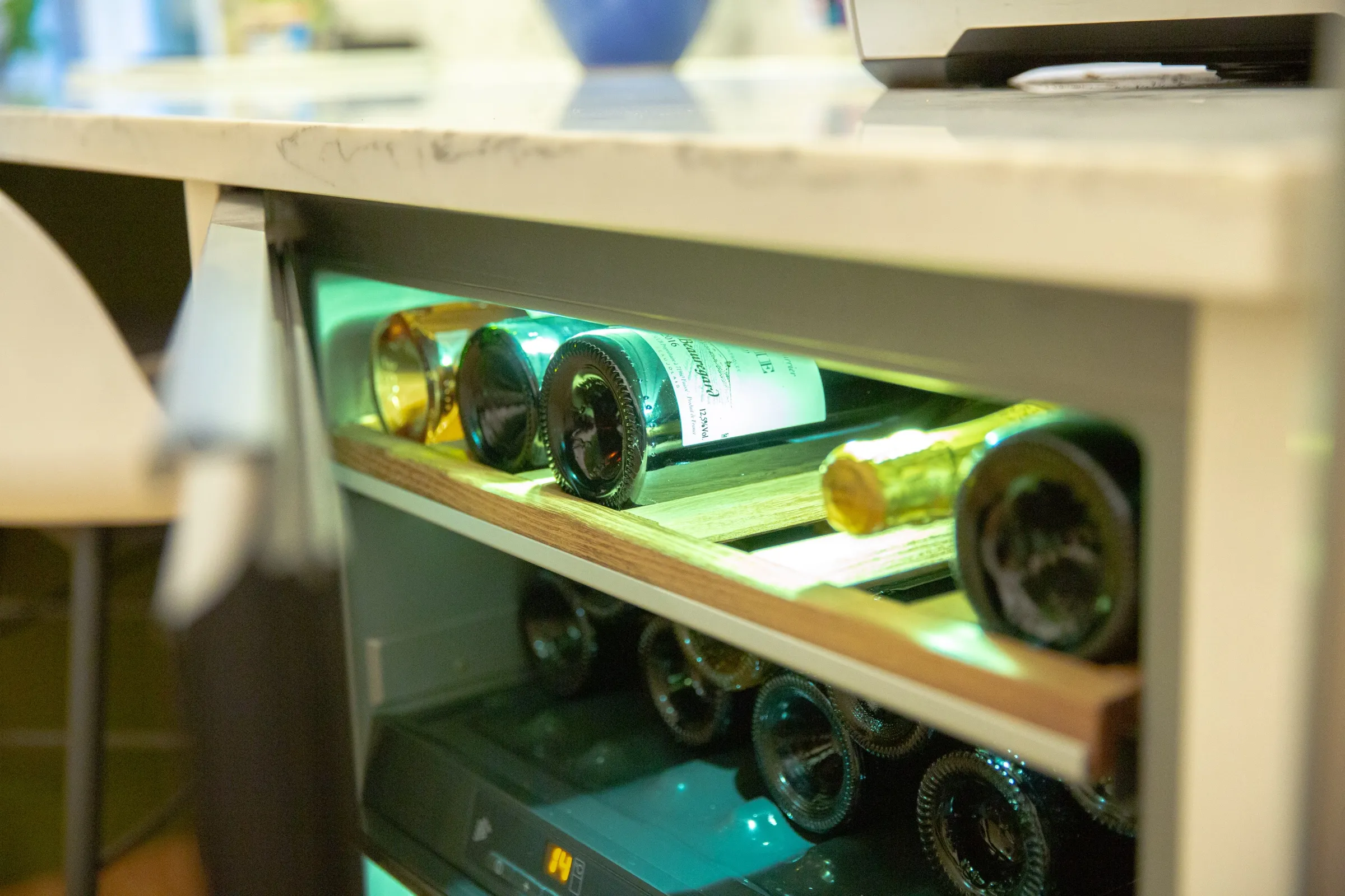 Close-up of the under-counter wine cooler, with bottles resting on an illuminated oak shelf
