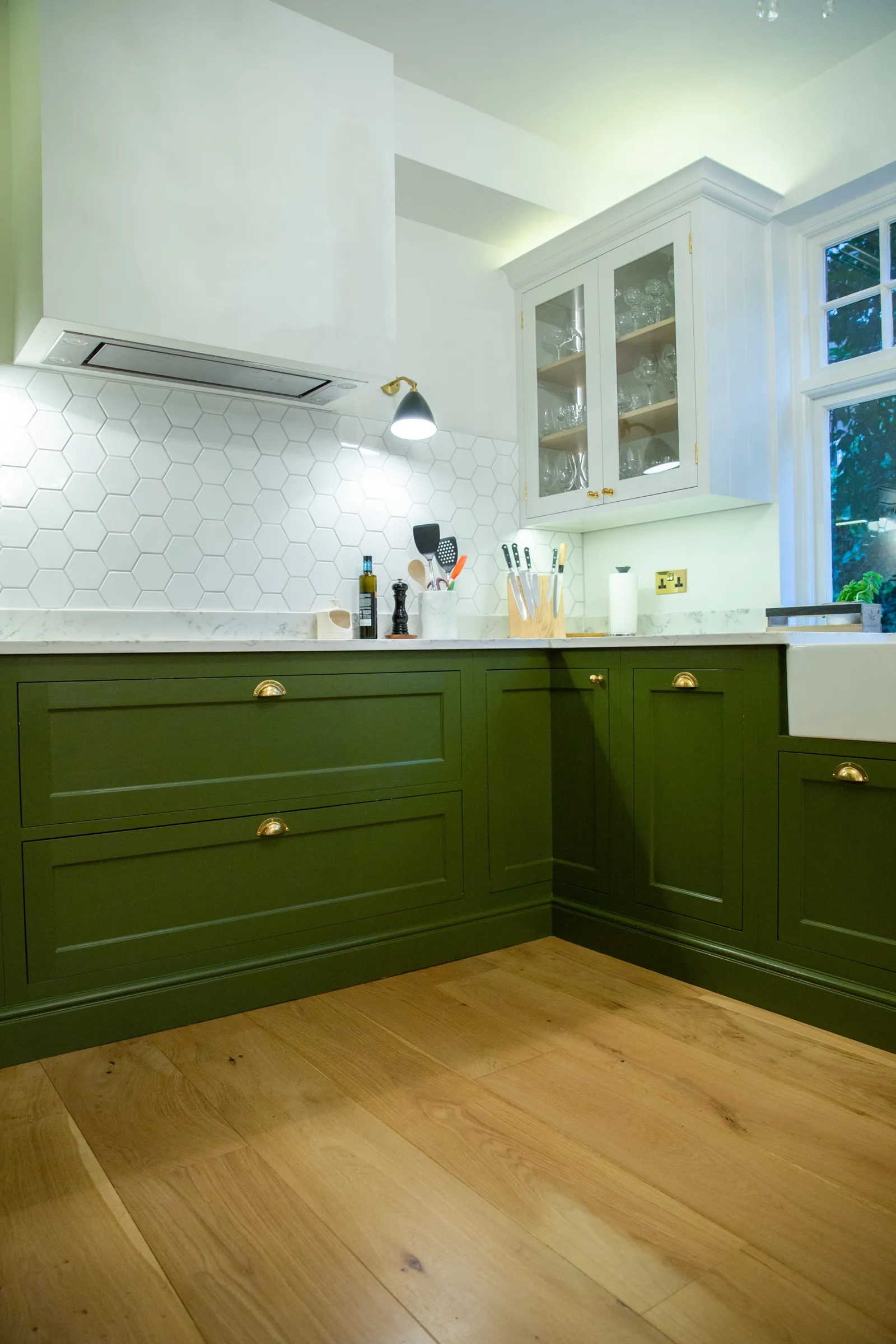 Green base drawers and cupboards beneath the white extractor hood, with a glazed display cabinet and the Belfast sink to the right