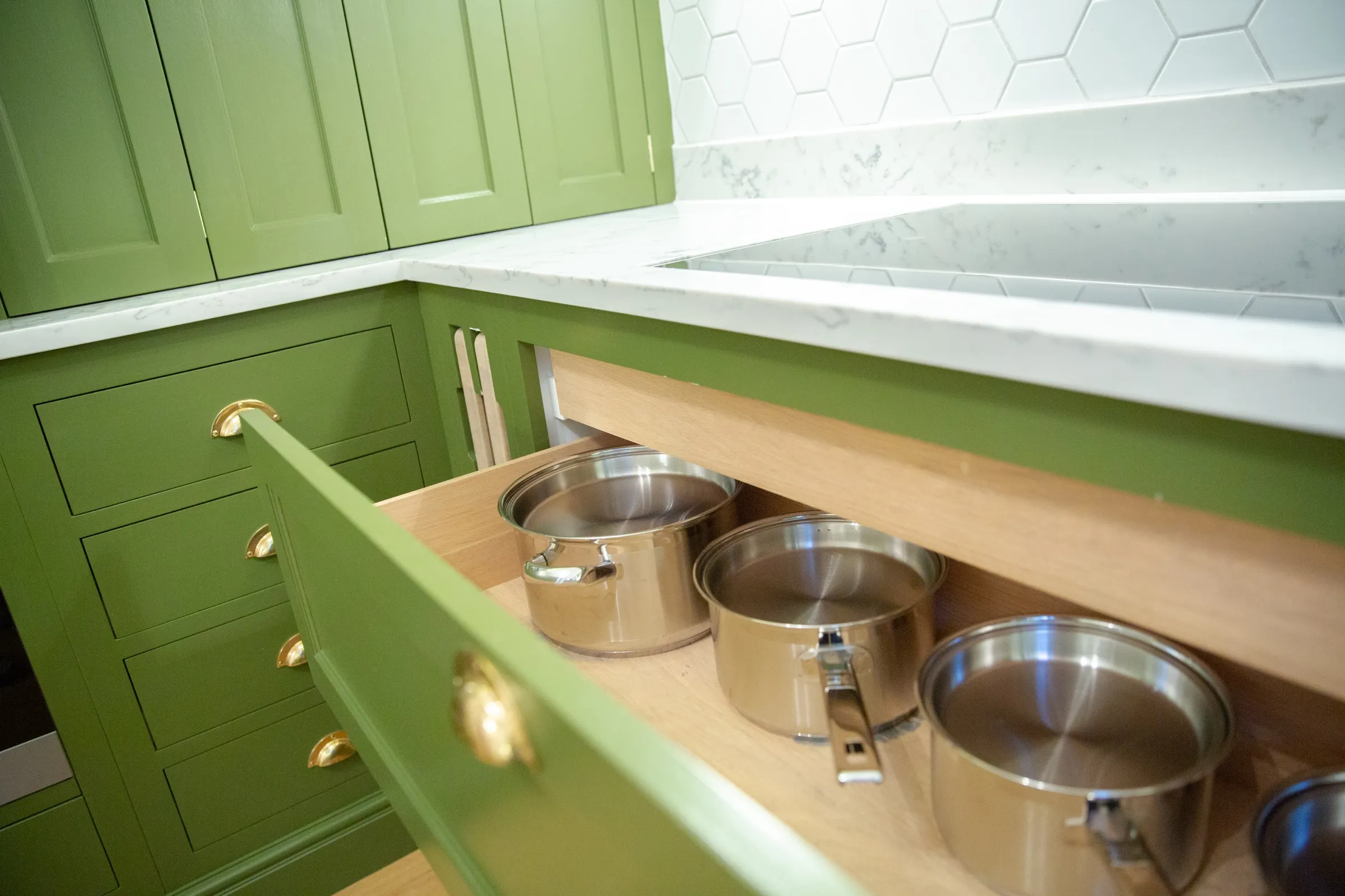 Deep oak-lined pan drawer pulled open to show stainless steel saucepans stored beside the hob