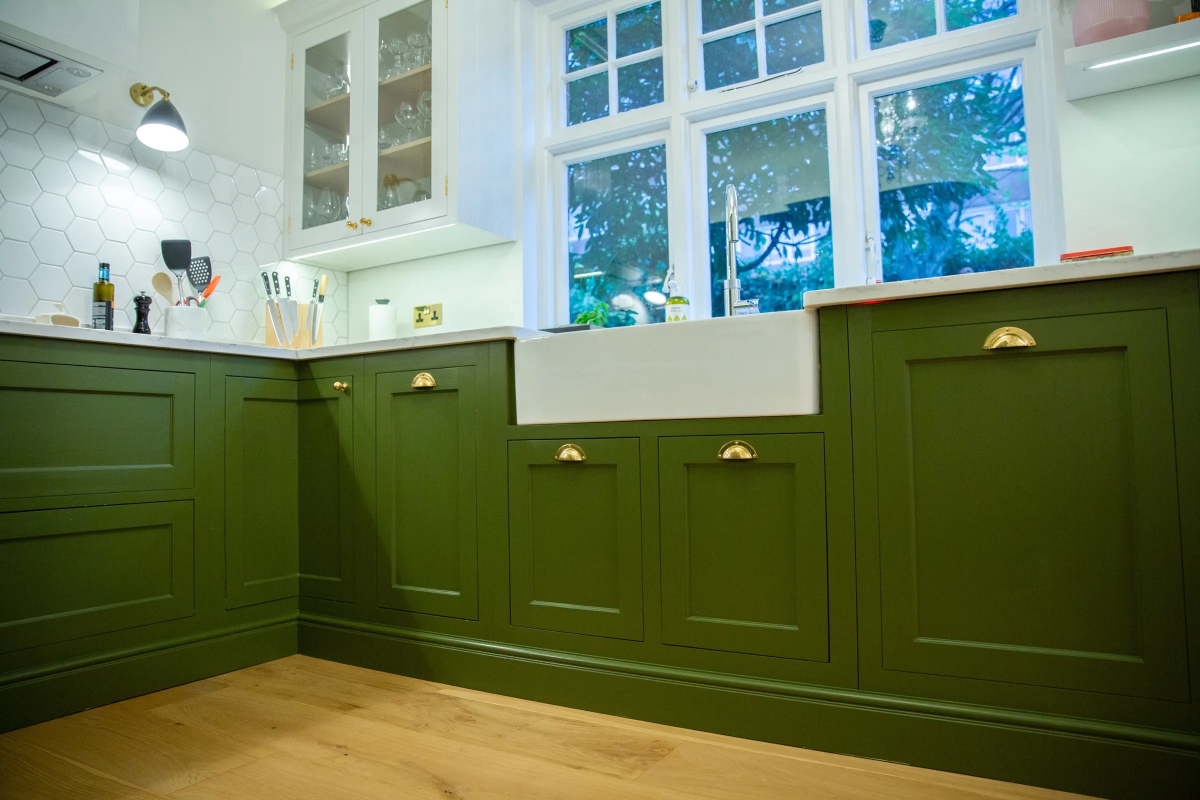 Belfast sink with chrome mixer tap set into the run of green cabinetry beneath white casement windows