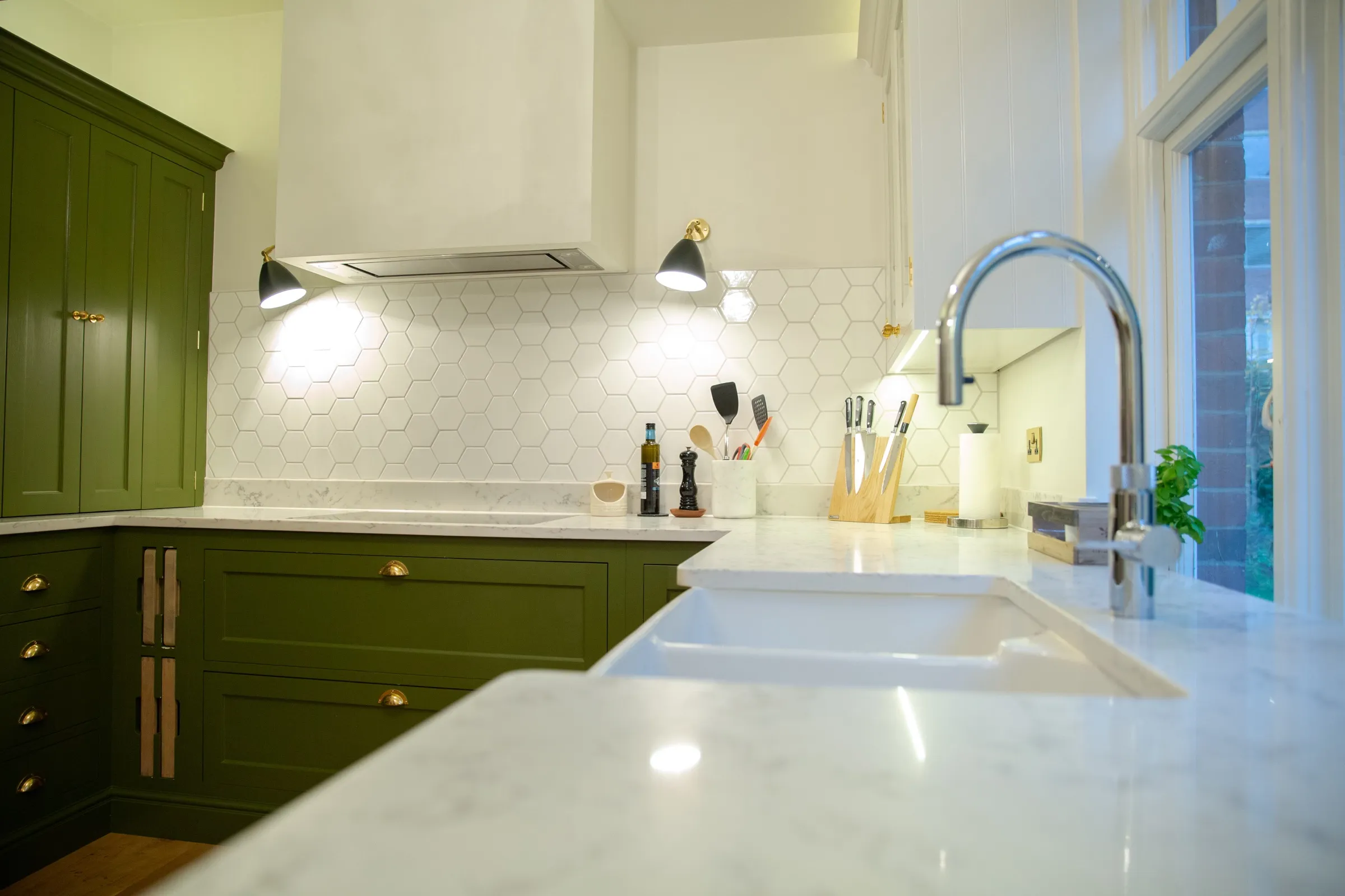Worktop-level view across the marble-effect quartz, past the double Belfast sink towards the hob and black wall lights