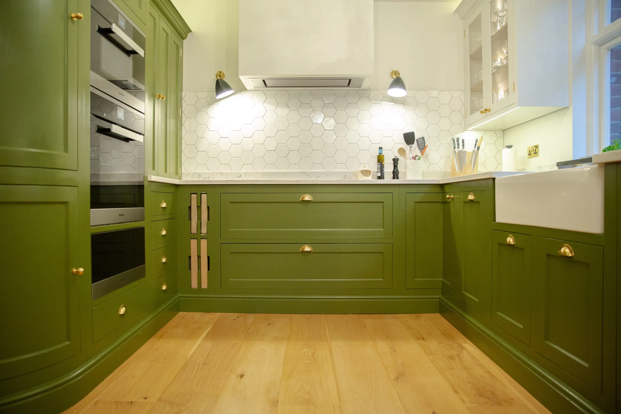 Wide view of the whole kitchen showing the curved oven cabinet, white hood, hexagon splashback and oak floor