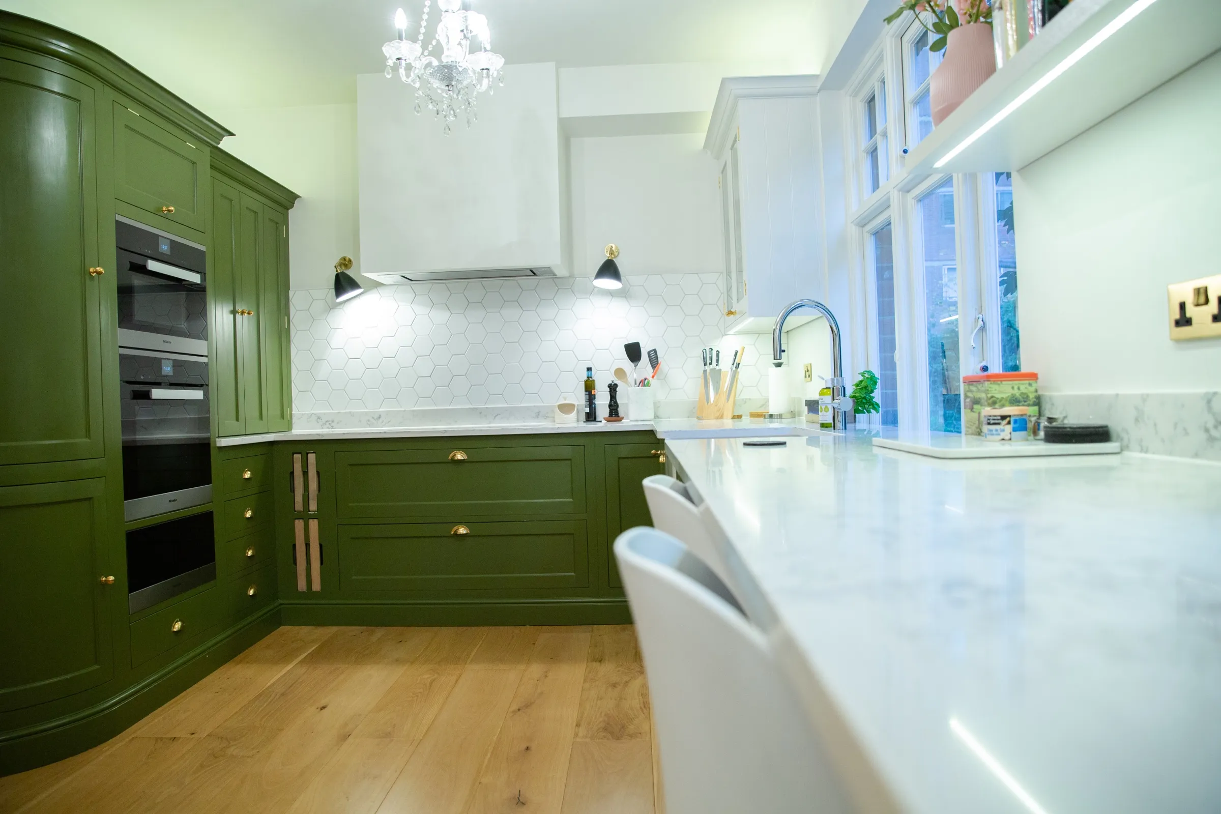 The kitchen seen from the breakfast bar end, with the quartz worktop sweeping towards the sink window and green cabinetry