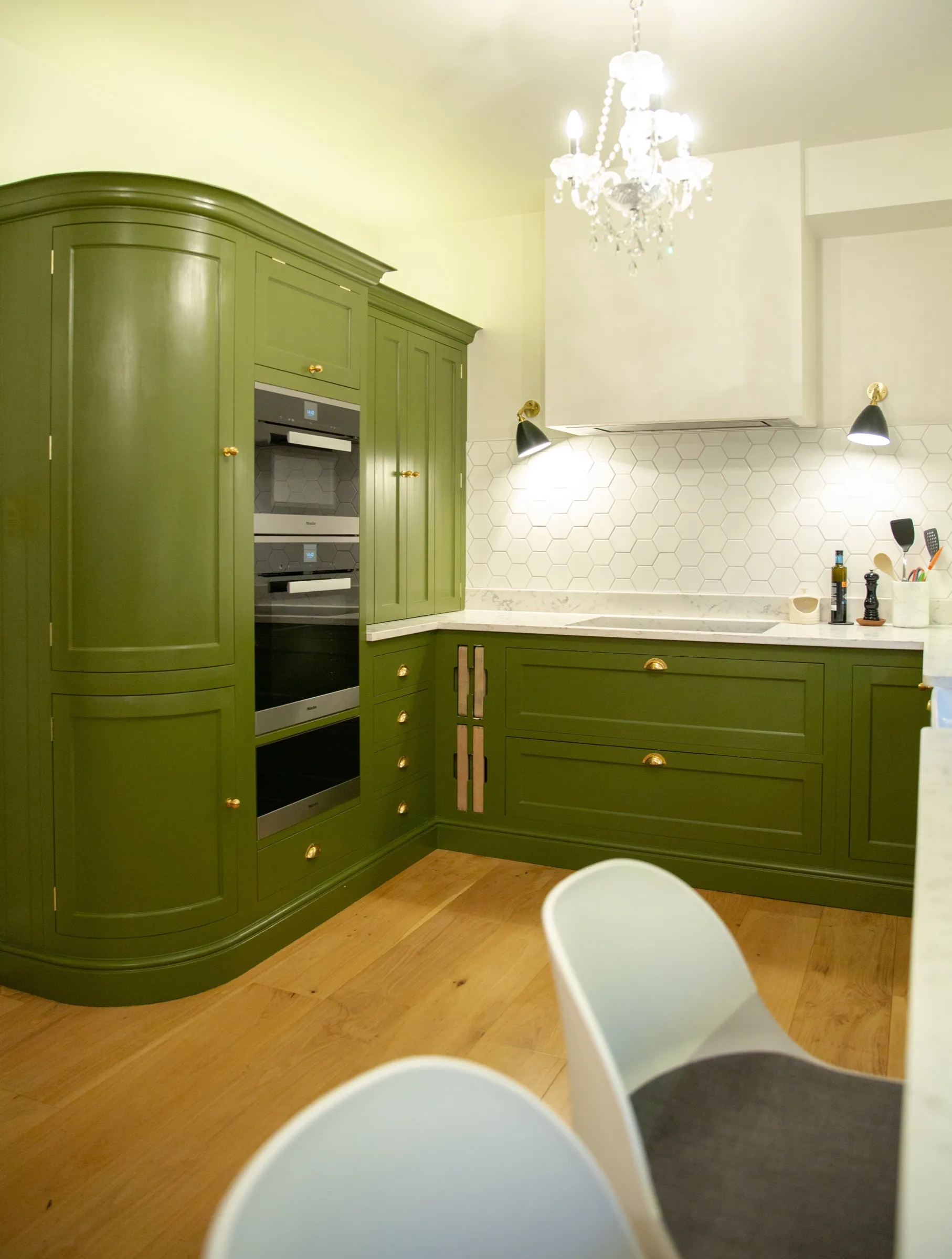 Curved hand-painted larder bank housing the stacked ovens, with the chandelier and breakfast bar in the foreground