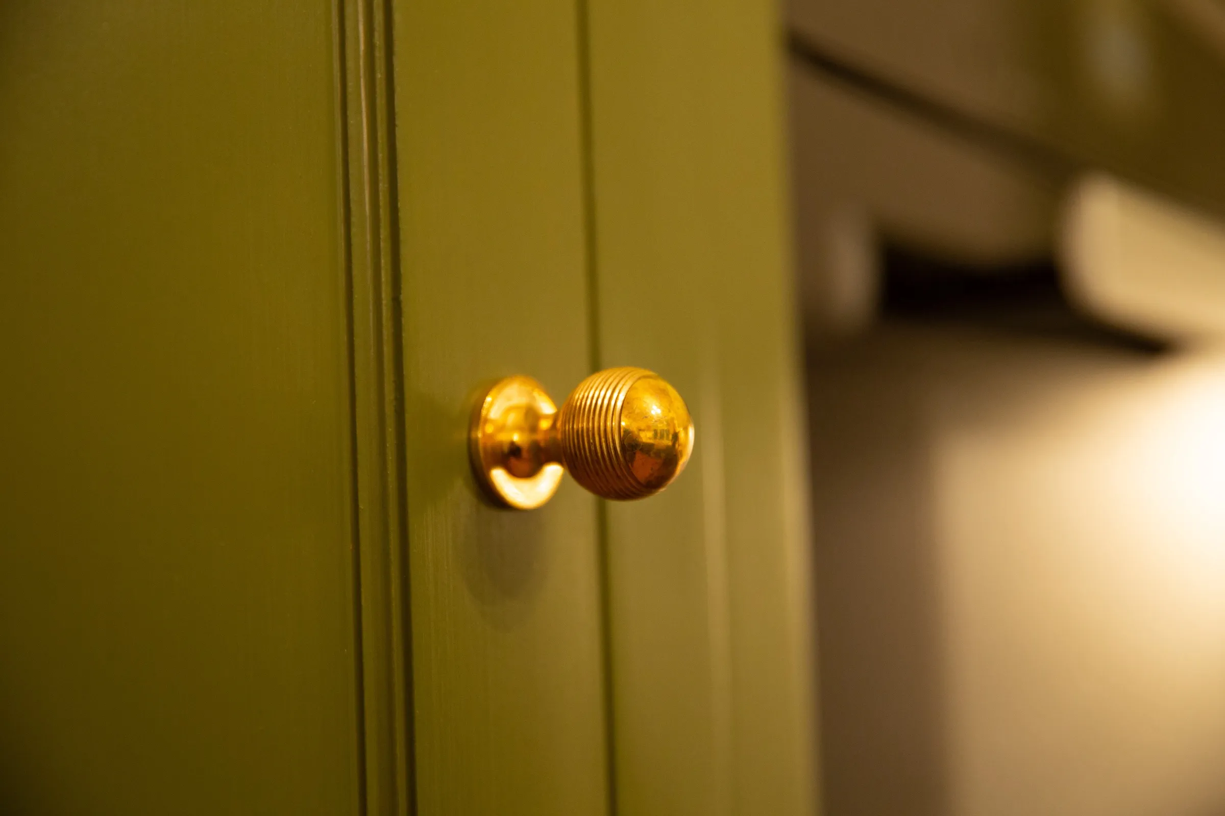 Close-up of a single reeded brass knob showing the brushed, hand-painted finish of the green door