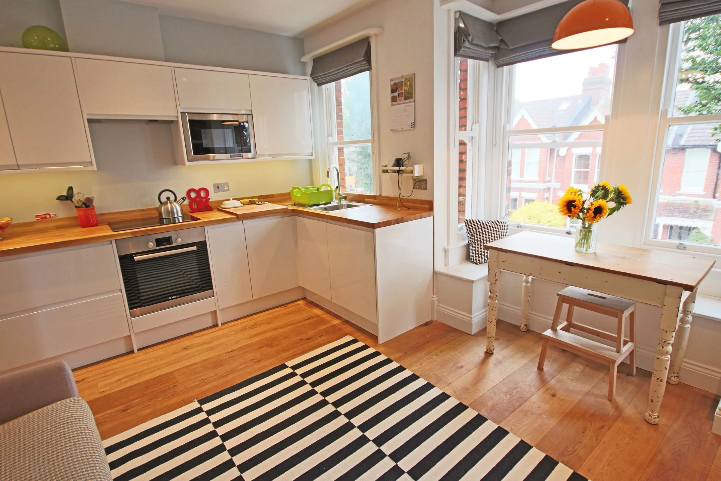 White handleless kitchen with solid oak worktops, built-in oven and integrated microwave, beside a bay window dining area with a vintage table and sunflowers