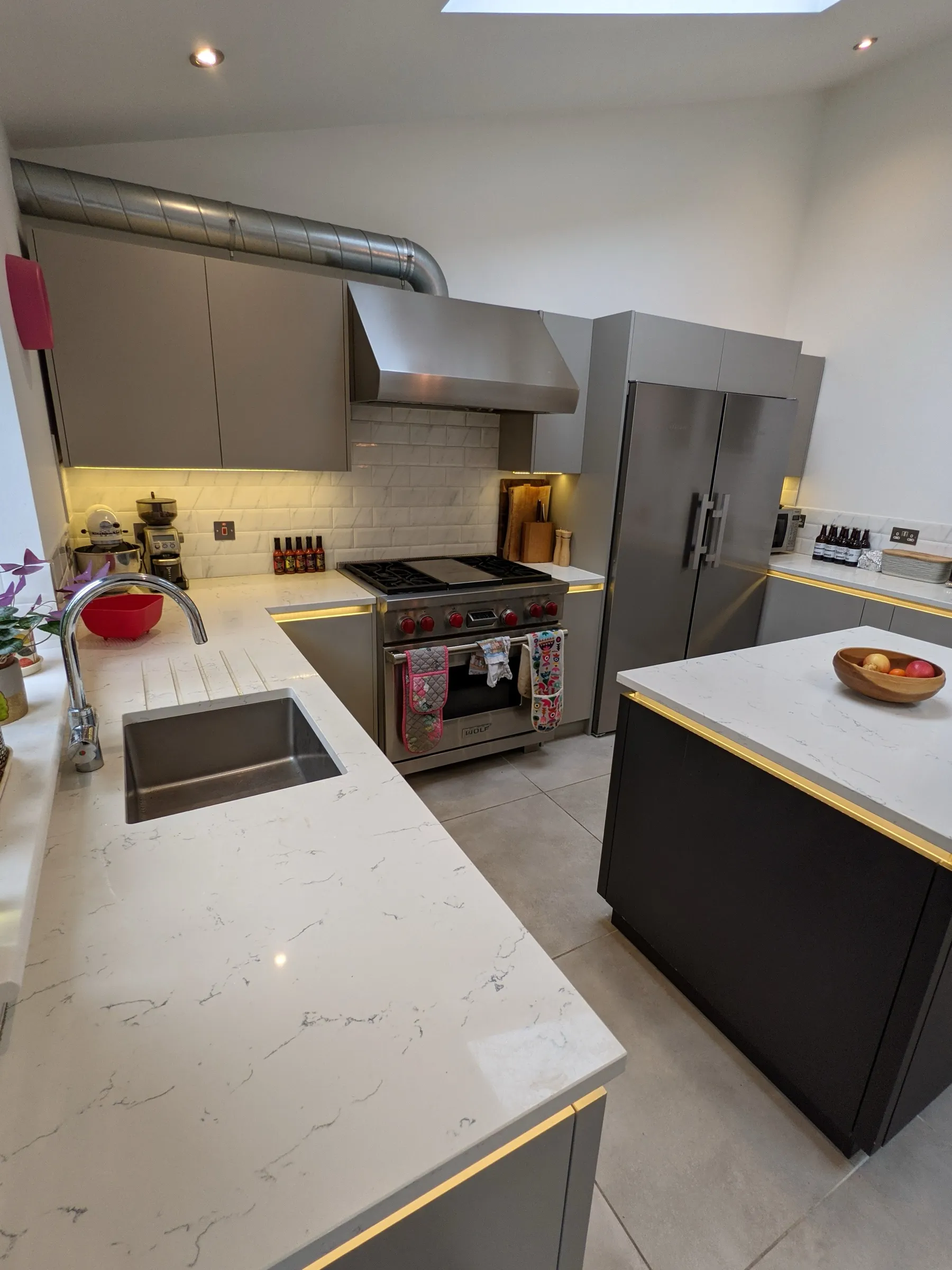 Quartz worktop with undermounted sink and drainer grooves, leading to a stainless range cooker with under-cabinet lighting