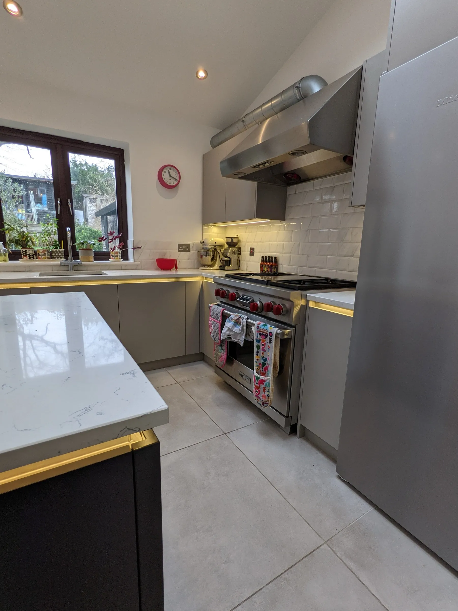 View past the charcoal island to the stainless range cooker, marble-effect metro splashback and garden window
