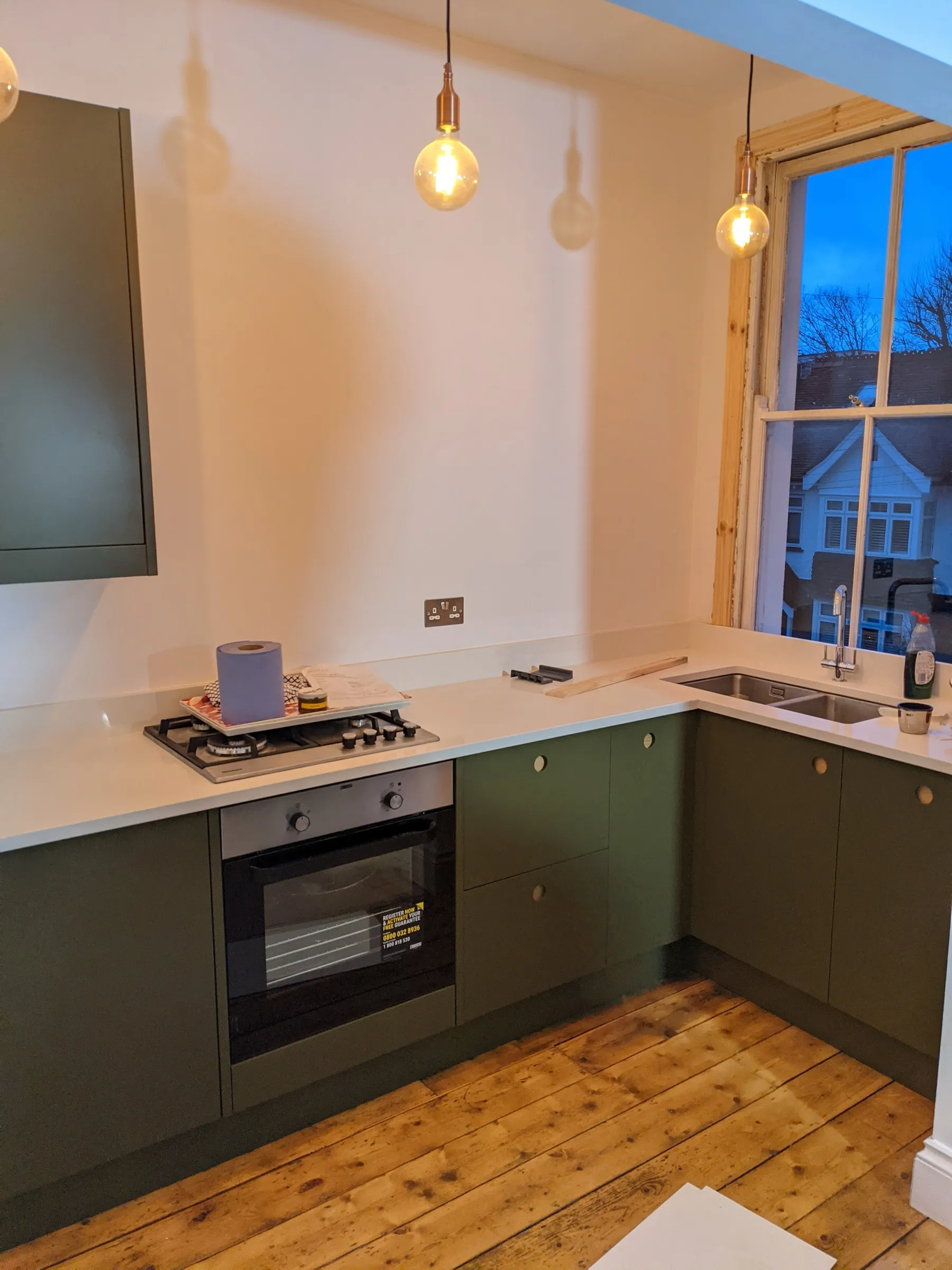 Olive green wall and base cabinets with circular timber pulls around a built-in oven and gas hob
