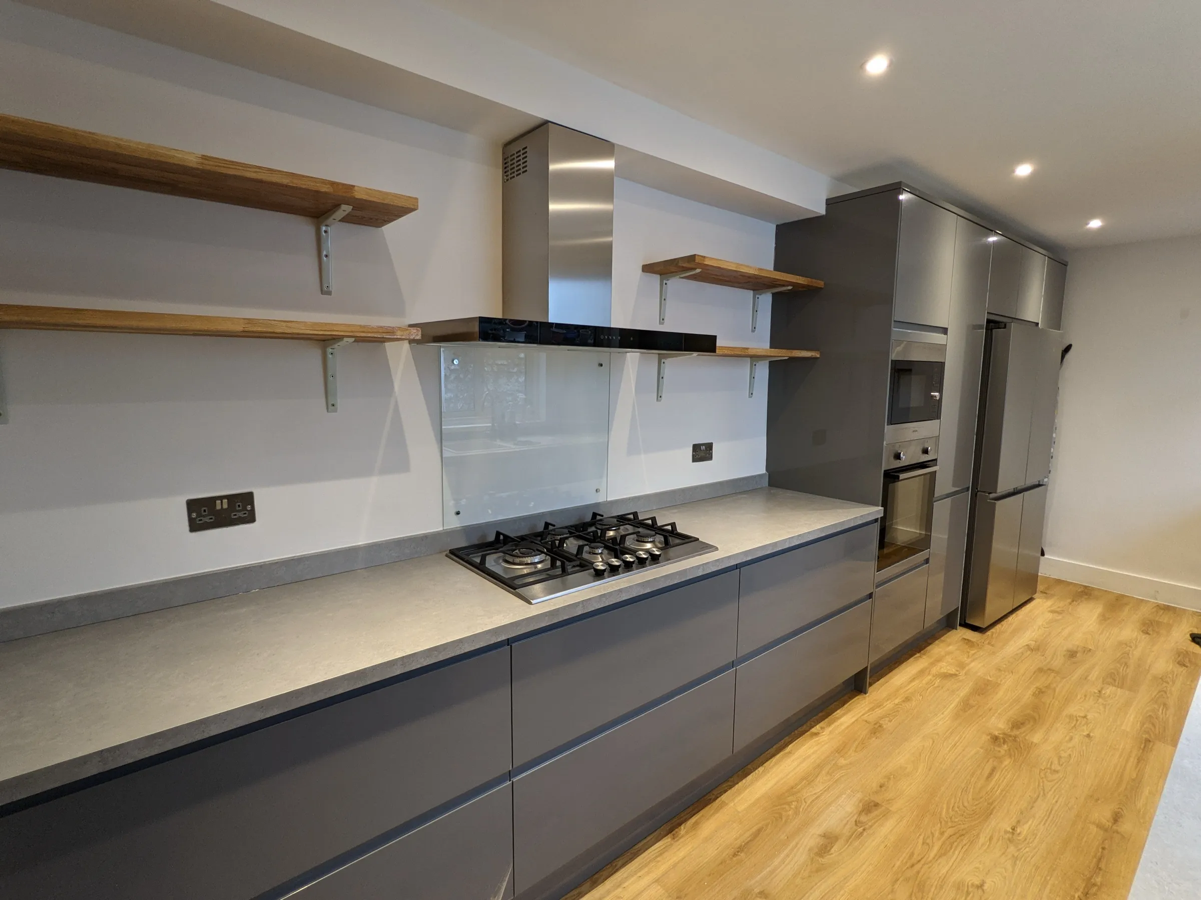 Long run of graphite gloss units with gas hob, glass splashback and tall housings with built-in ovens