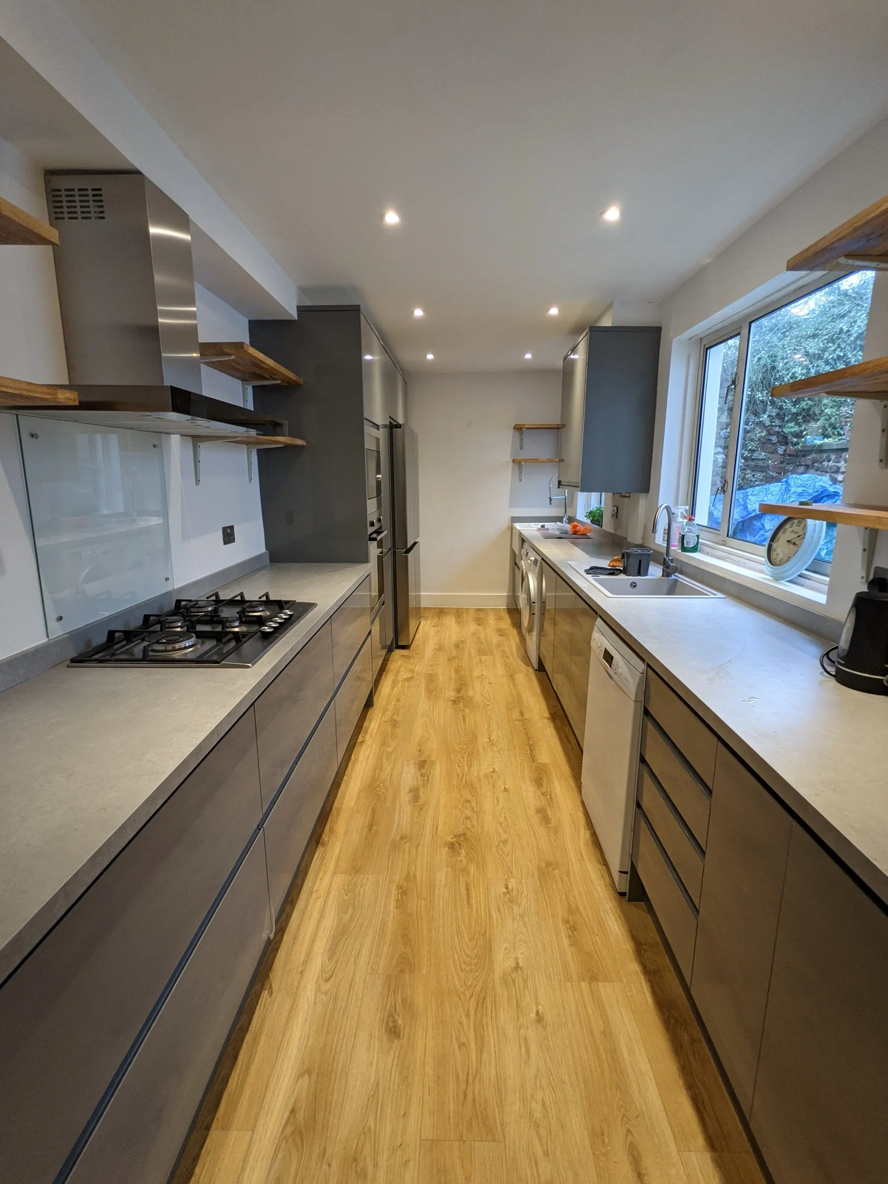 Graphite gloss galley kitchen seen from the hob end, looking towards the window, sink and dishwasher