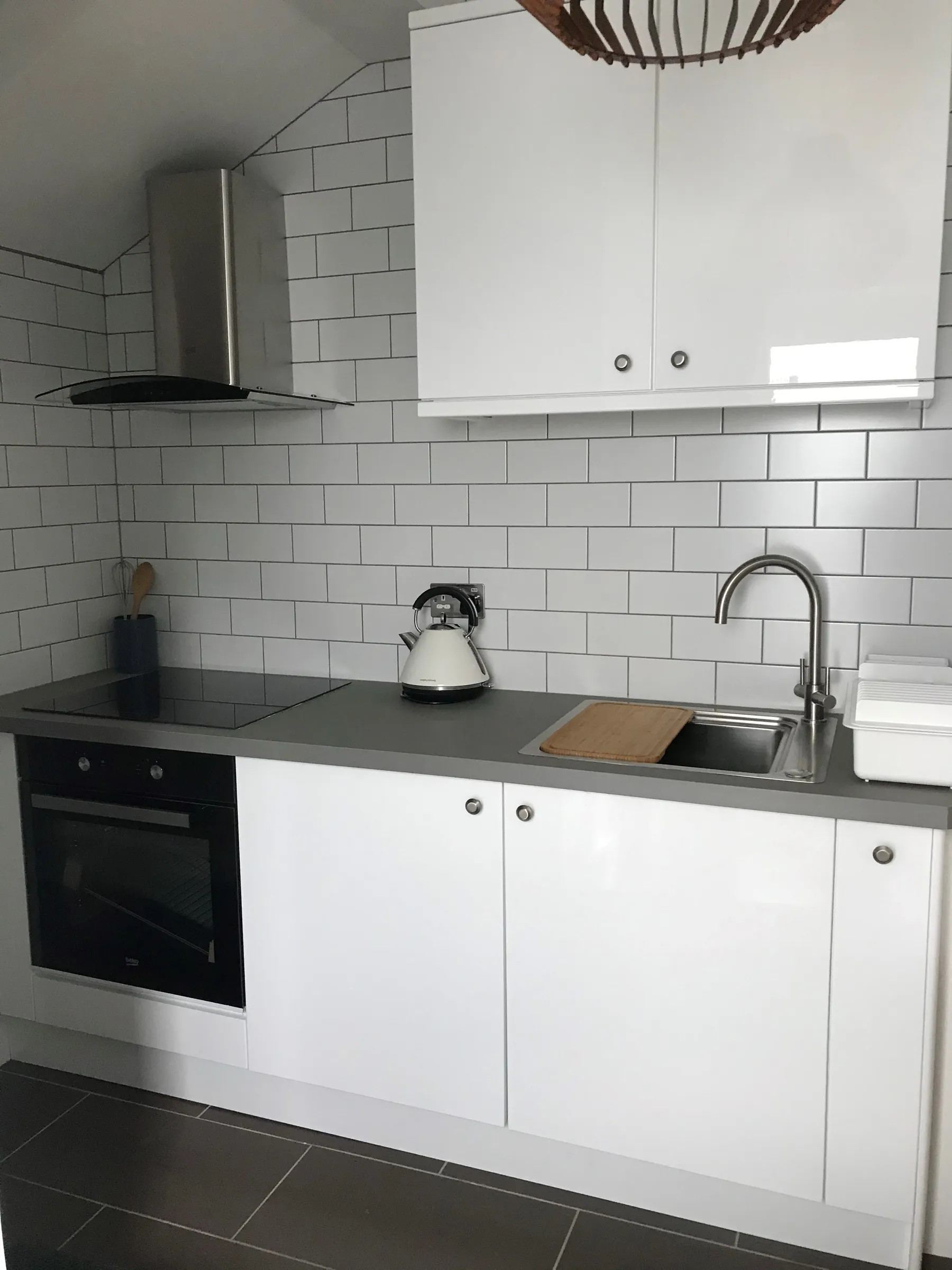 Compact white gloss kitchen with metro tiles, slate grey worktop, black built-in oven and curved glass hood