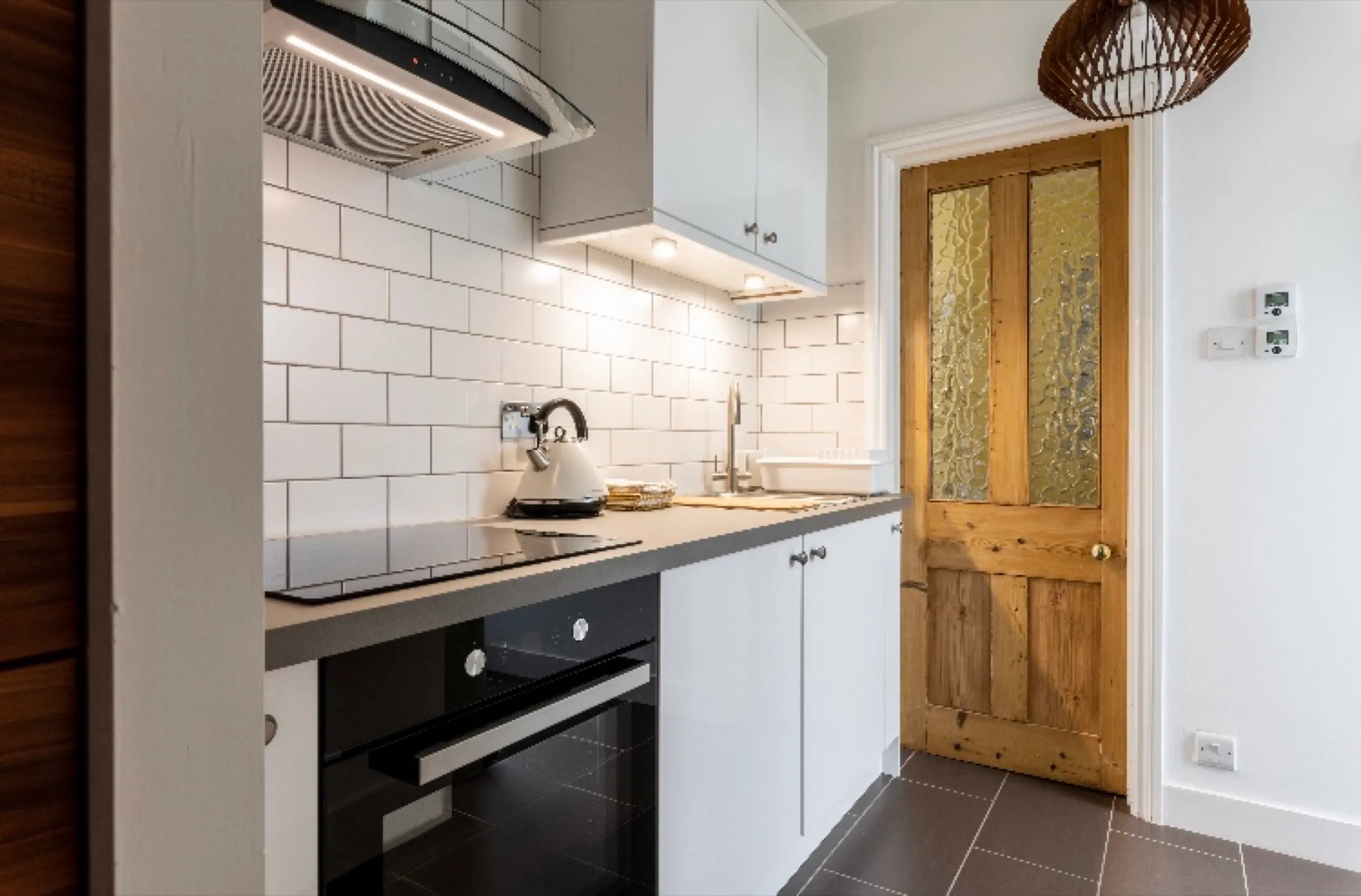 White gloss kitchen with metro tiles and grey worktop beside a stripped pine door with patterned glass