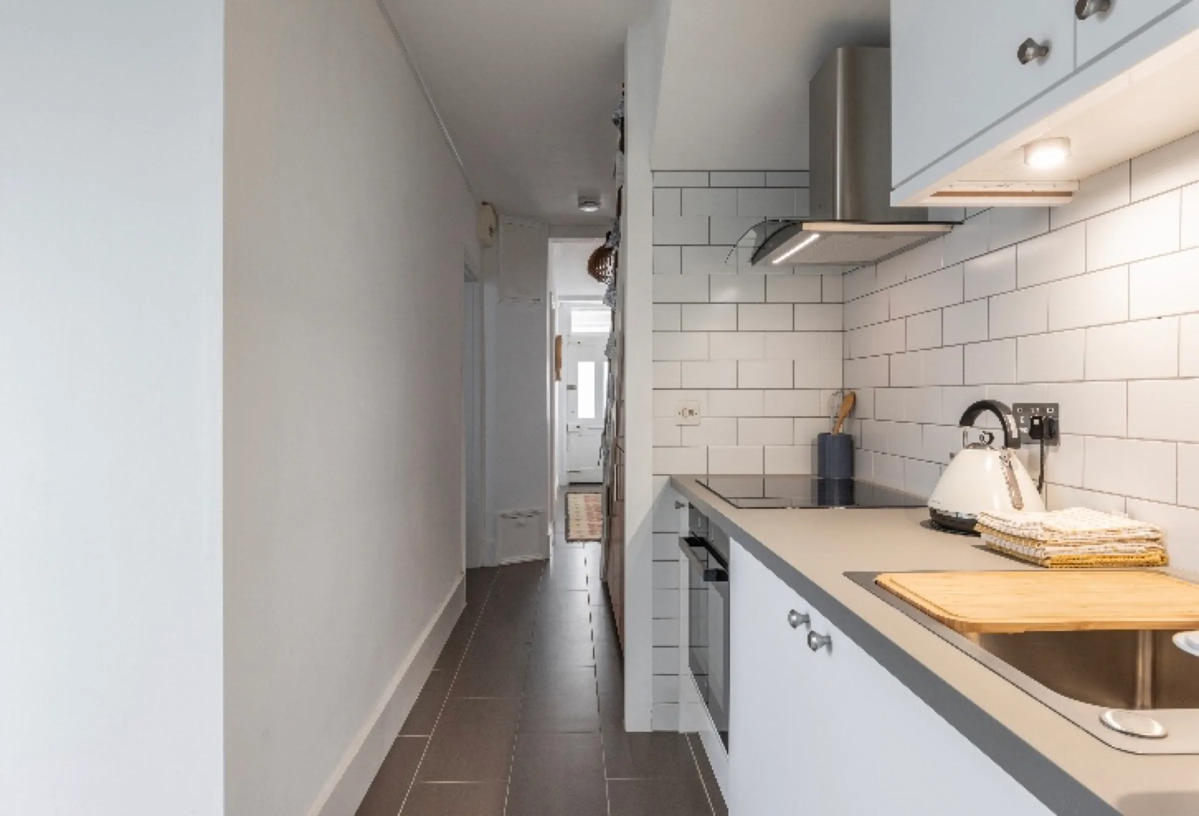 Galley view of the white gloss kitchen with under-cabinet lighting, ceramic hob and stainless sink