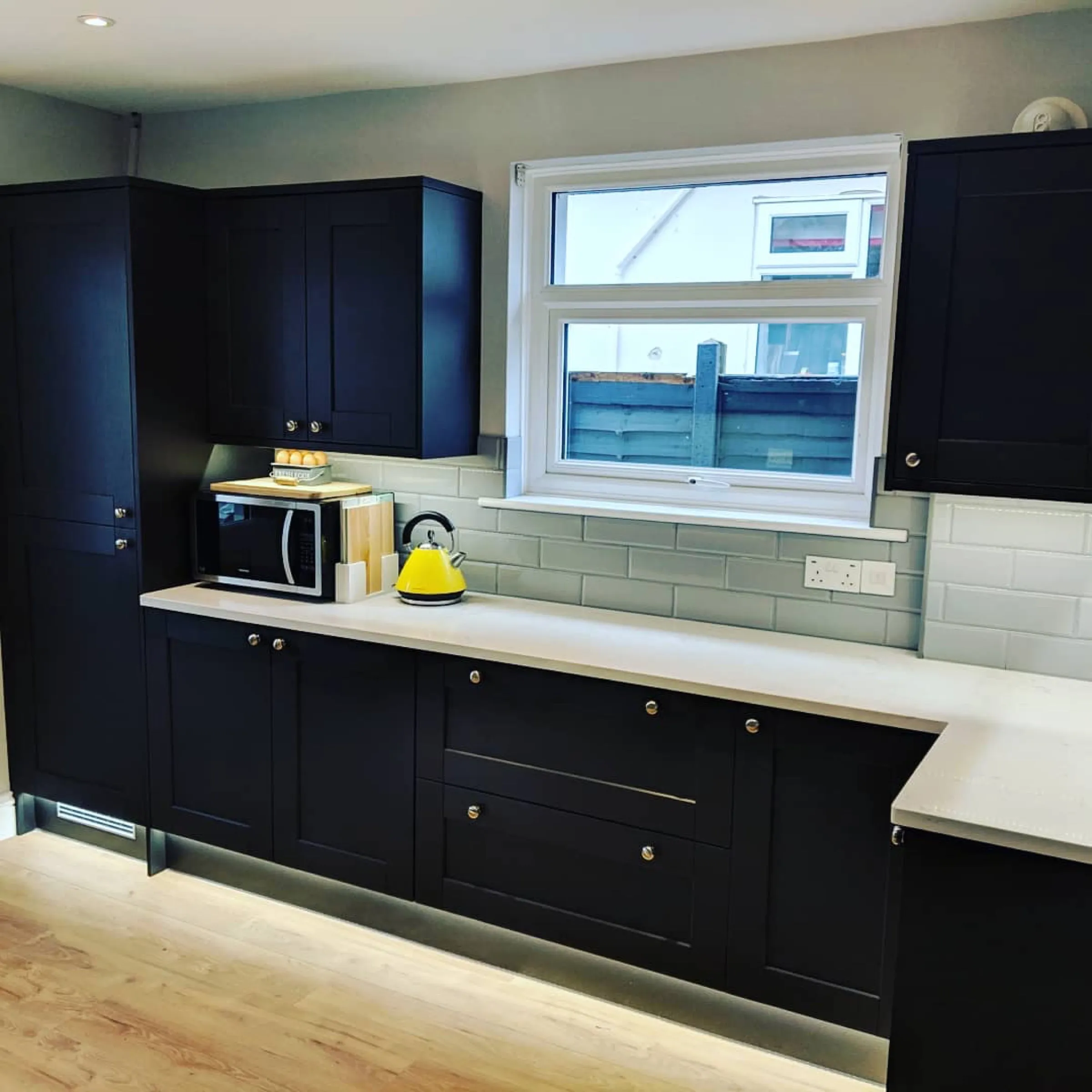 Navy Shaker kitchen with white quartz worktops, pale grey metro splashback and warm plinth lighting