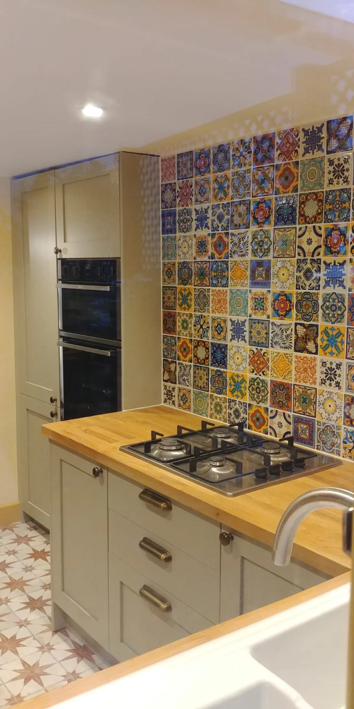 Sage green Shaker kitchen with oak worktop, gas hob and colourful Mexican patchwork tile splashback