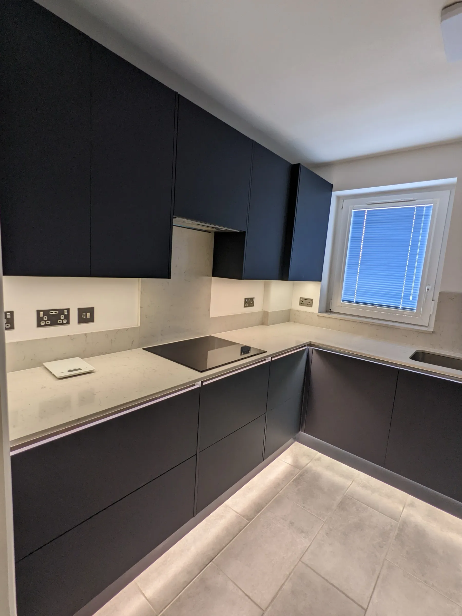 Hob run of the matt black kitchen with induction hob, quartz splashback upstands and LED plinth lighting