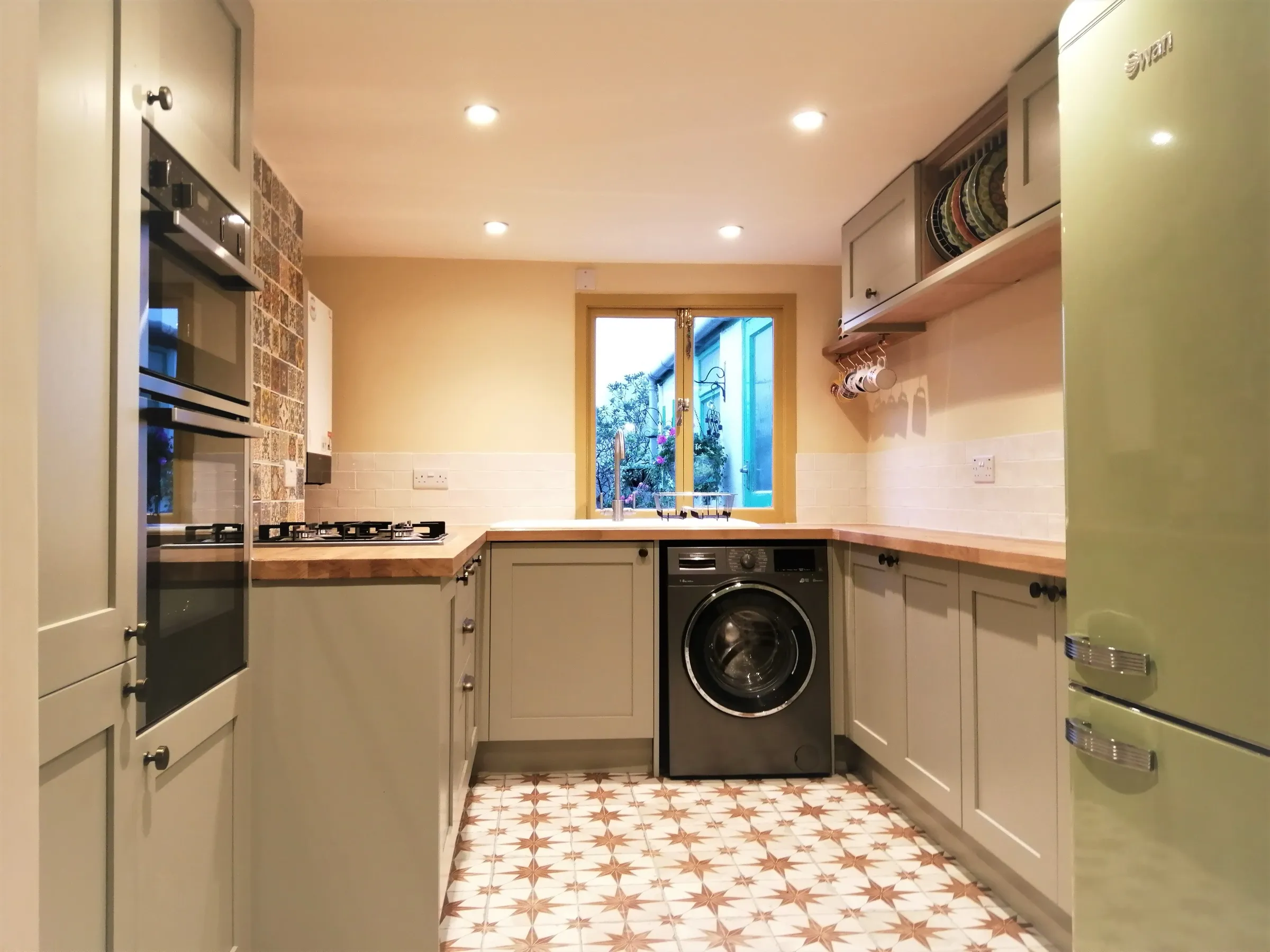 Sage green Shaker galley with oak worktops, star-patterned floor tiles and retro green fridge-freezer