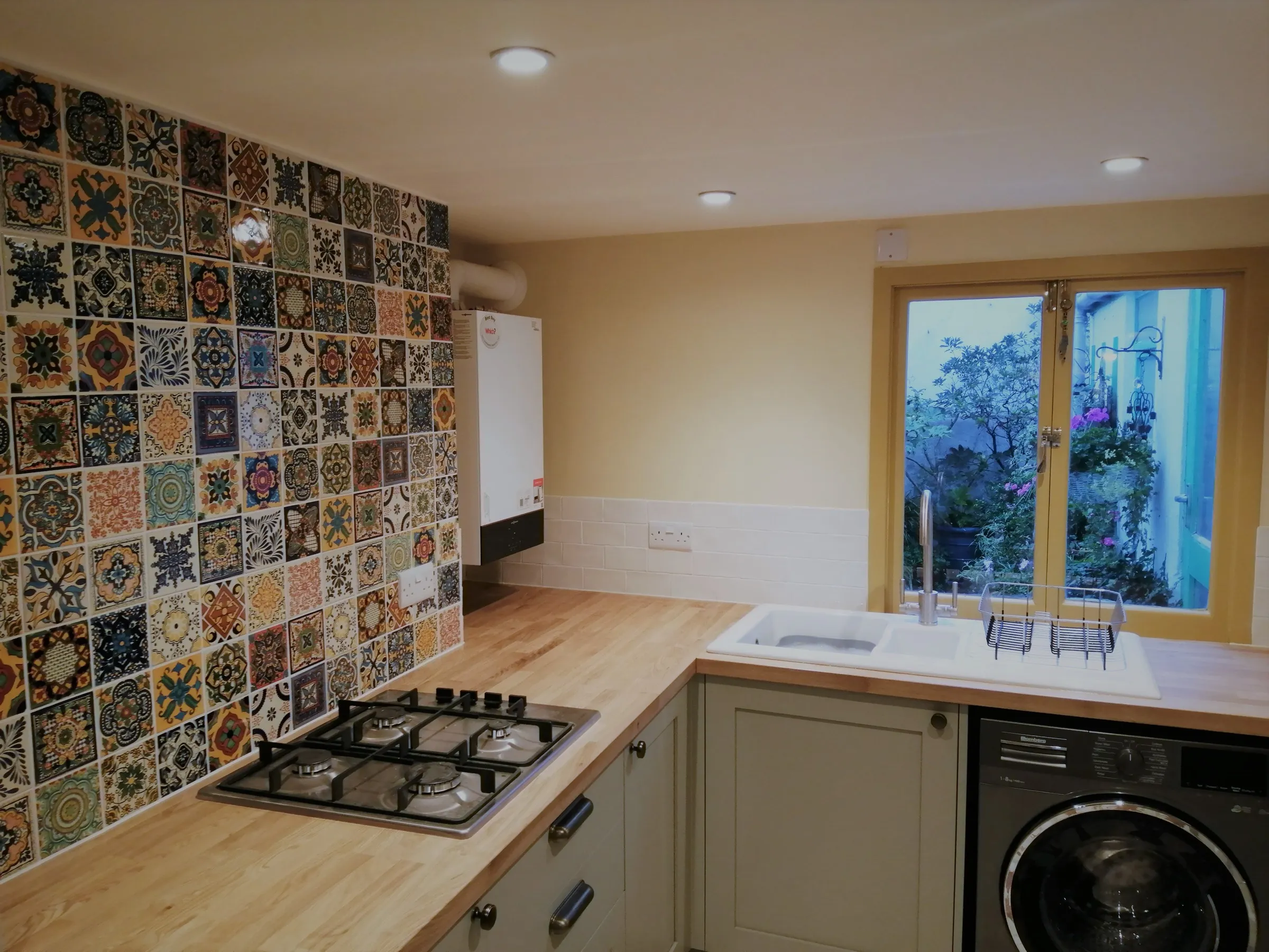 Oak worktops, four-burner gas hob and Mexican patchwork tiles beside a white ceramic sink and garden window
