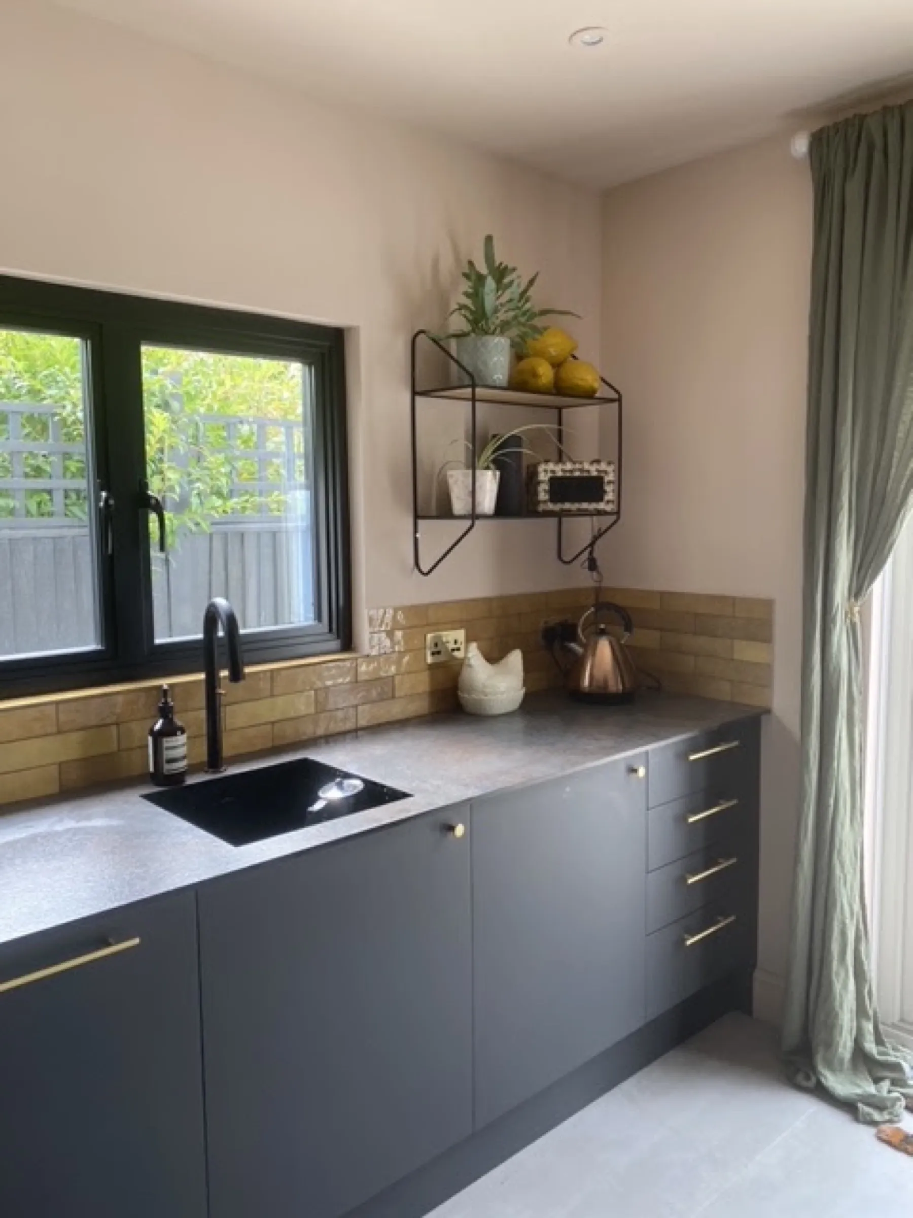 Charcoal cabinets with slim brass handles, black composite sink and matt black tap against an amber glazed-brick splashback