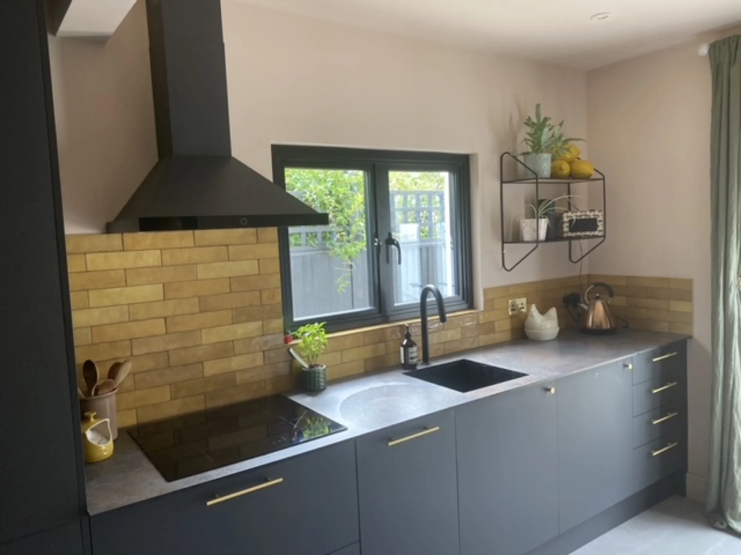 Charcoal kitchen with black chimney hood, induction hob, stone-effect worktop and honey-toned brick splashback