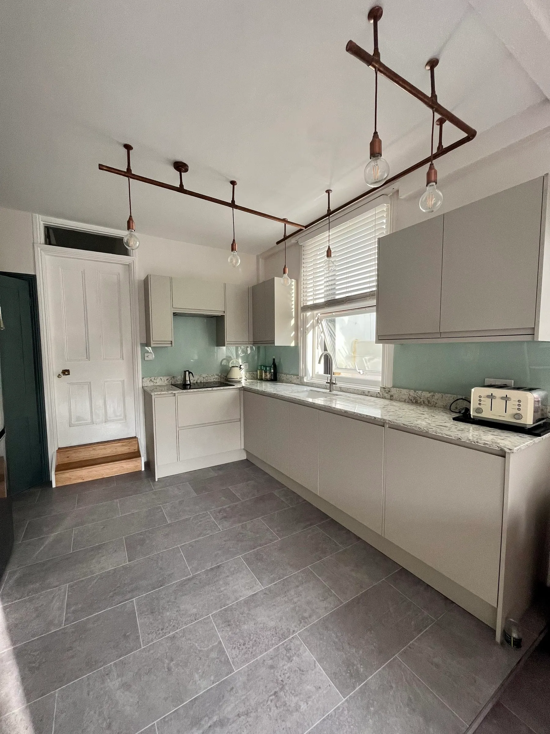 Cashmere handleless kitchen with granite worktops, aqua glass splashback and bespoke copper-pipe lighting rails
