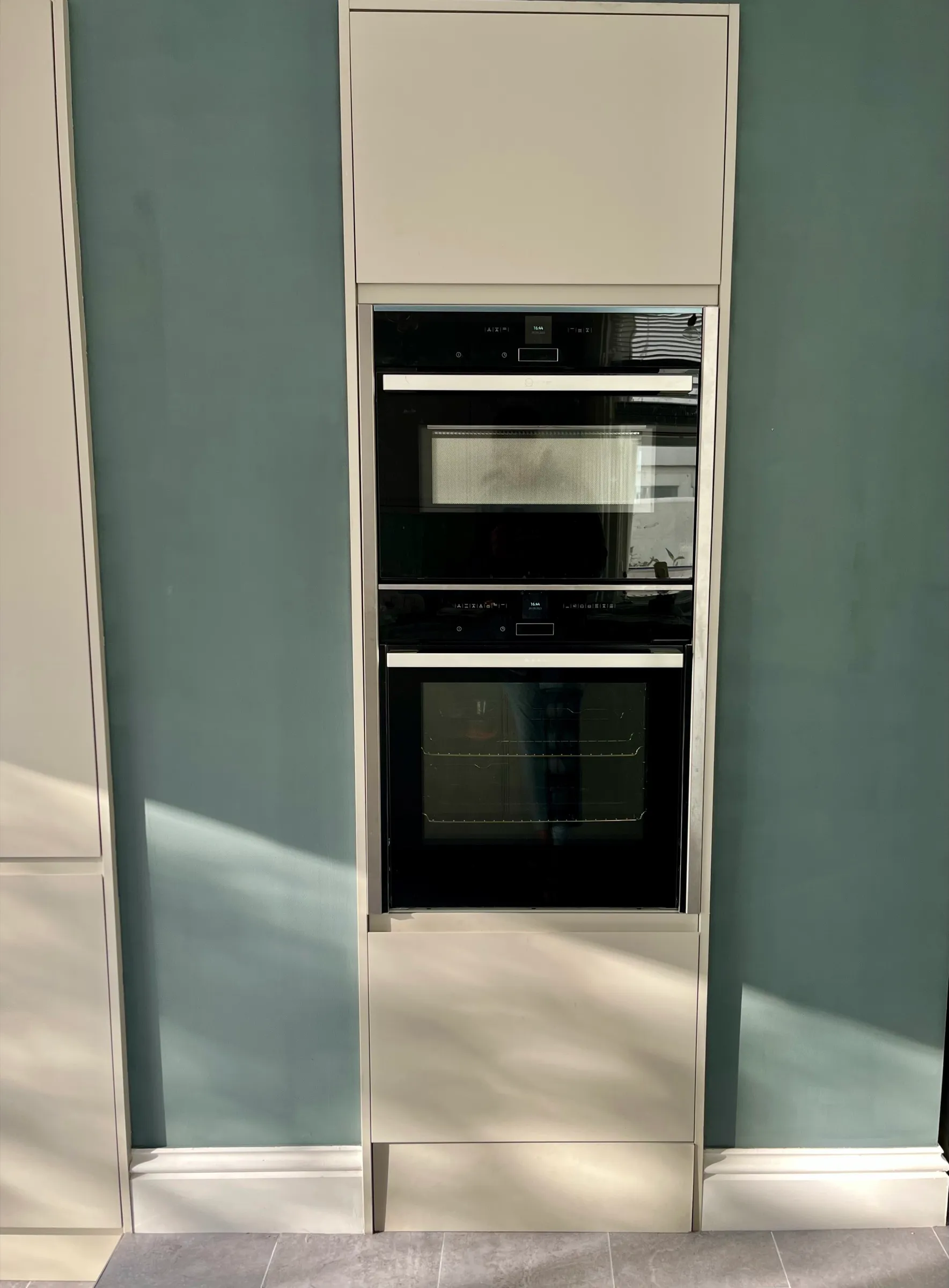 Tall cashmere housing with stacked ovens set into a deep teal feature wall