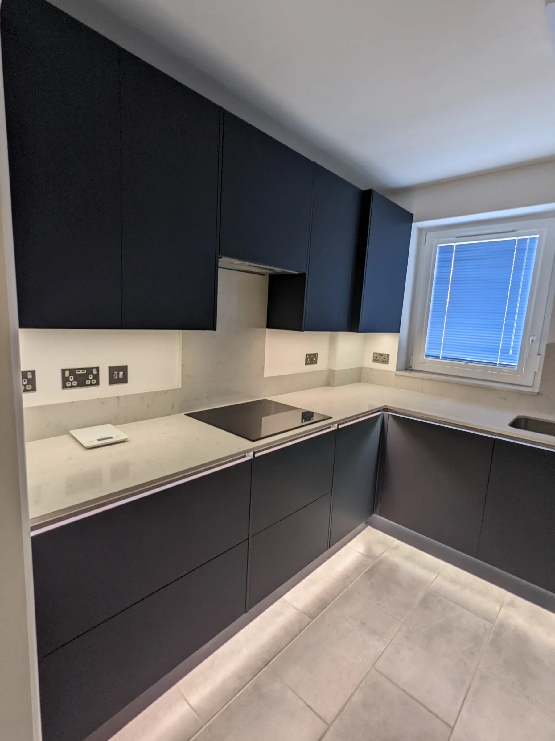 Dark matt handleless kitchen with induction hob, marble-effect quartz worktops and under-cabinet lighting