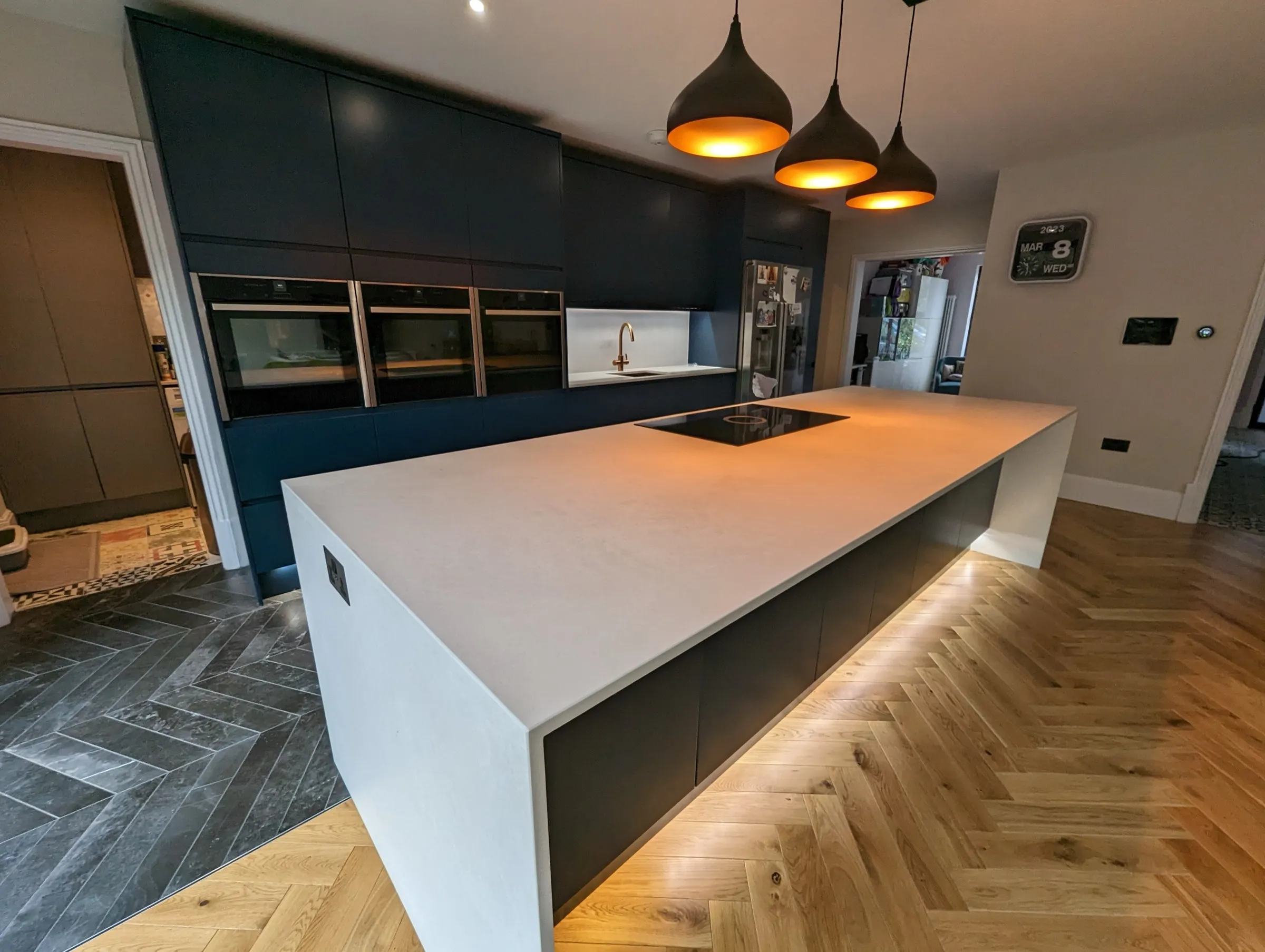 Navy handleless kitchen with white stone island, induction hob and copper-lined pendant lights