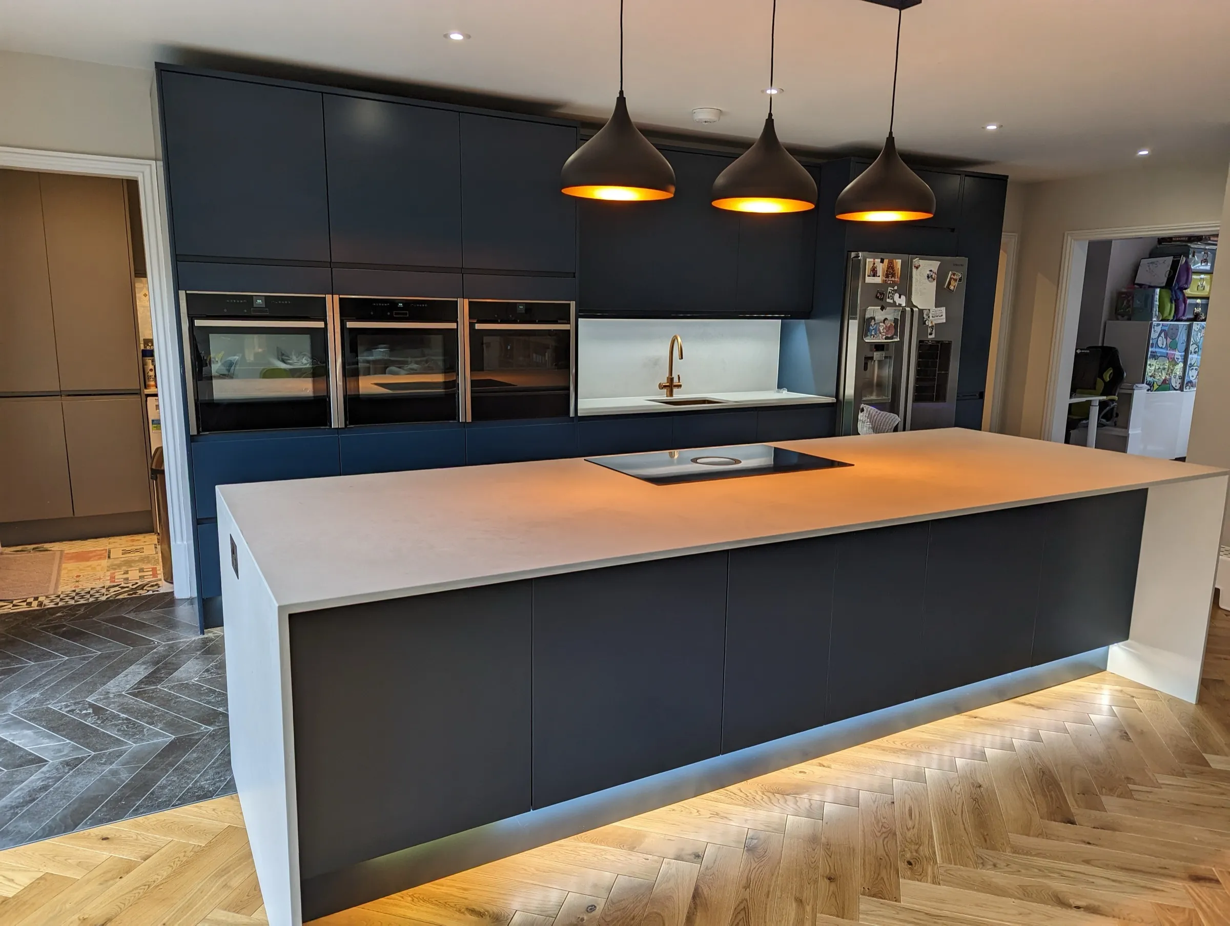 Full-width view of the navy cabinetry, triple ovens and floating white island with under-lighting