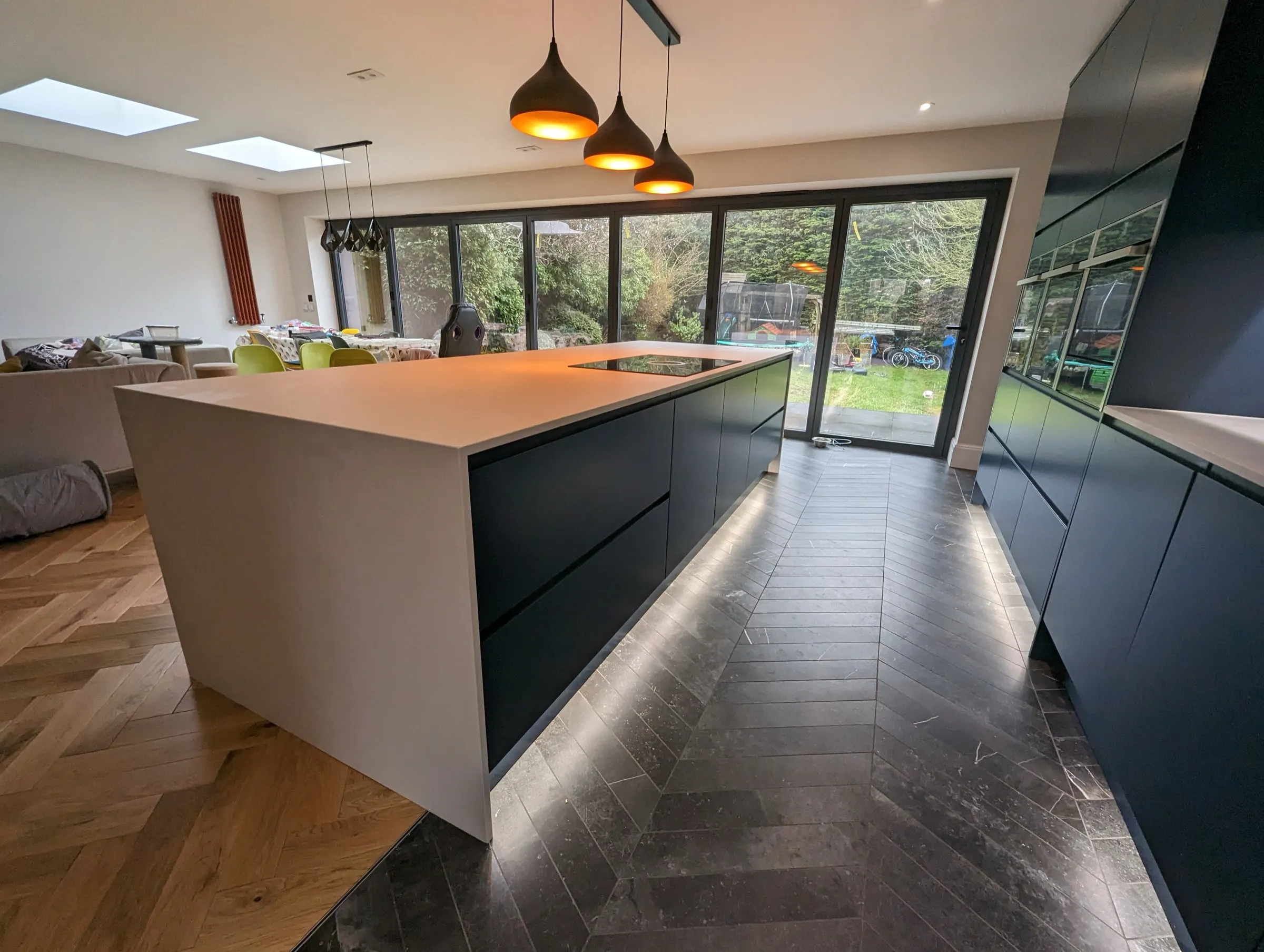 Navy kitchen with white island, American-style fridge freezer and oak-to-slate flooring transition
